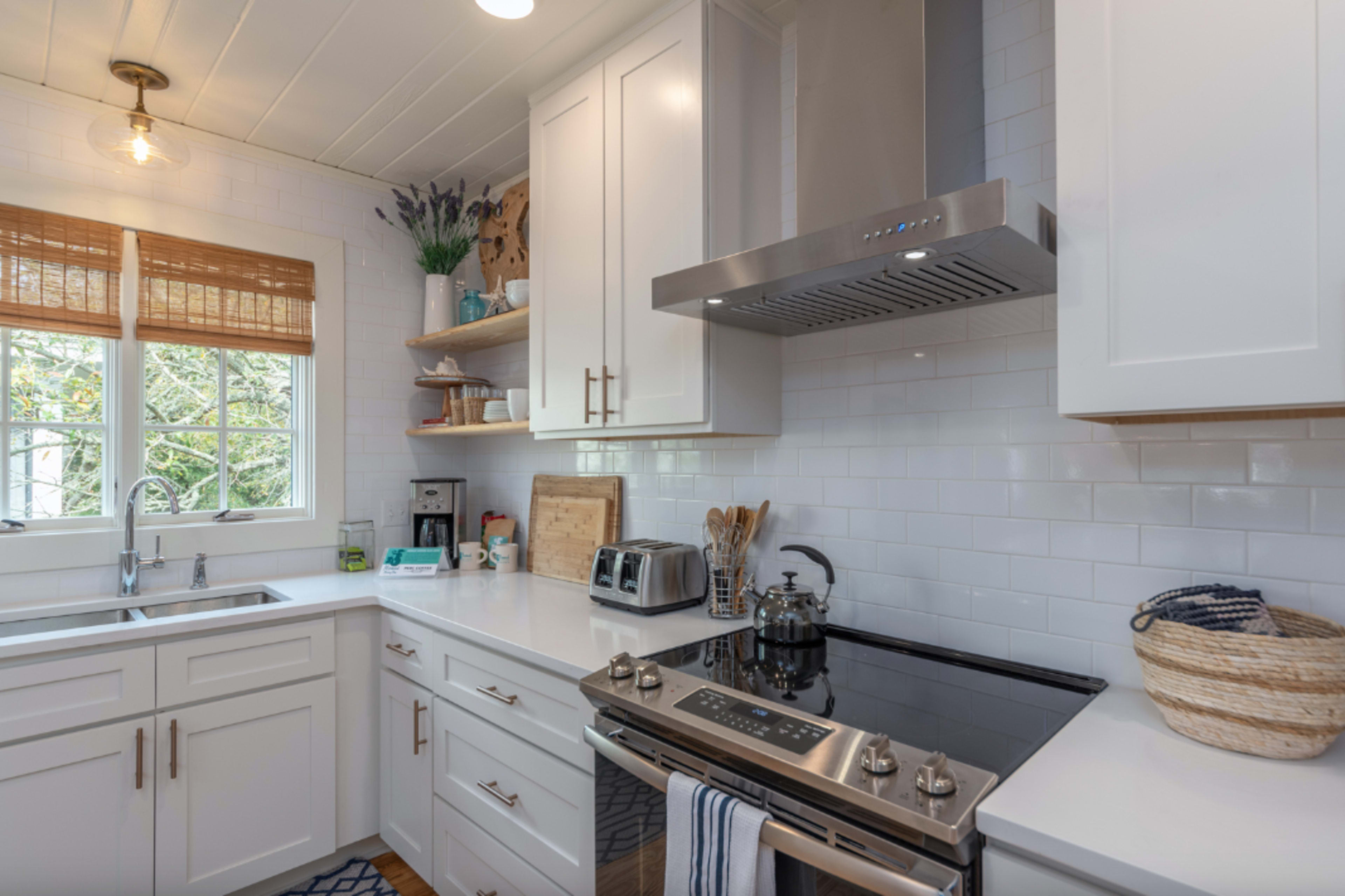 A modern kitchen features white cabinets, a stainless steel stove, and natural light streaming through a window.