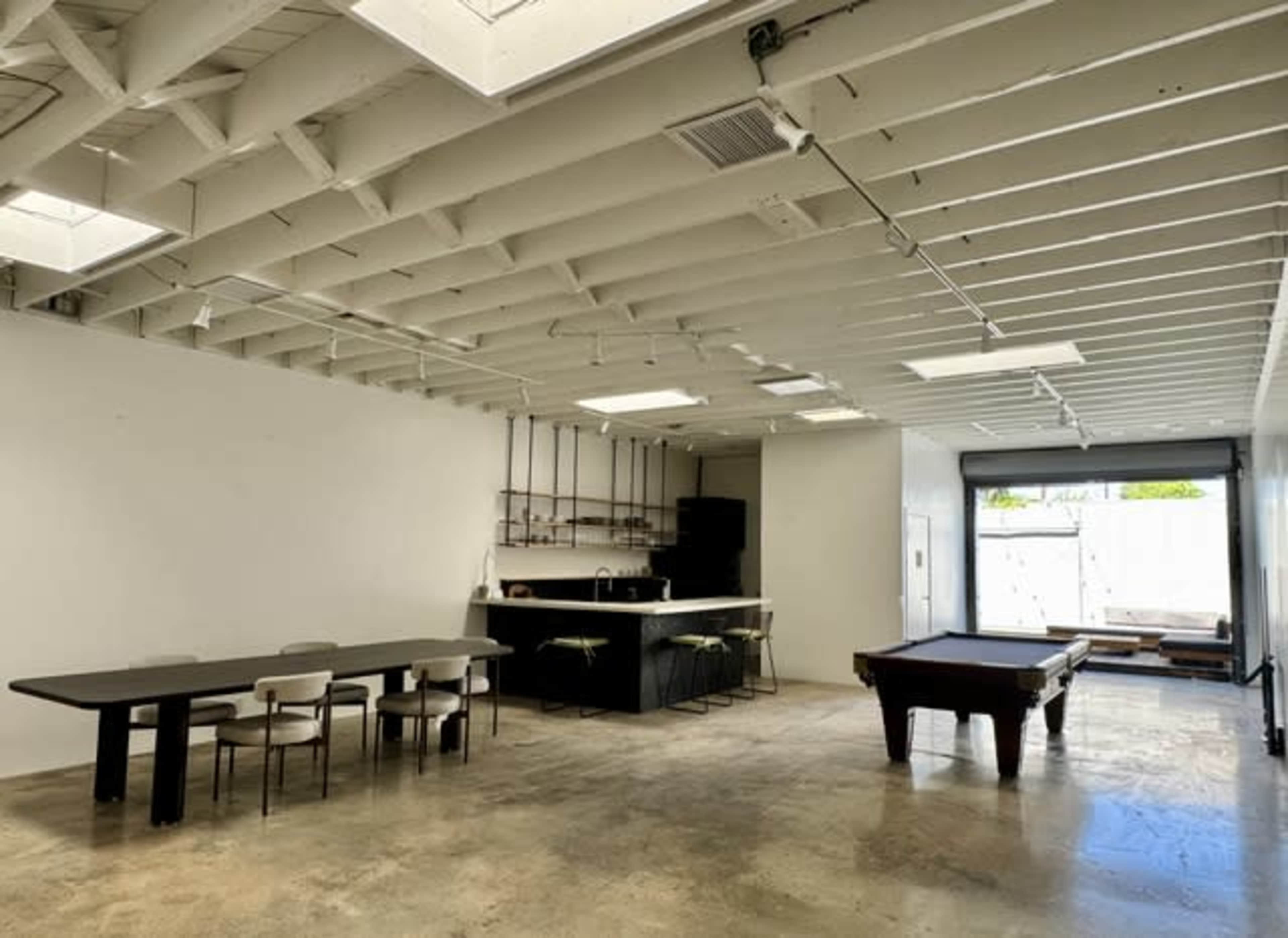 The image shows a spacious interior with a dining table, kitchen area, and a pool table, all under a ceiling with exposed beams.