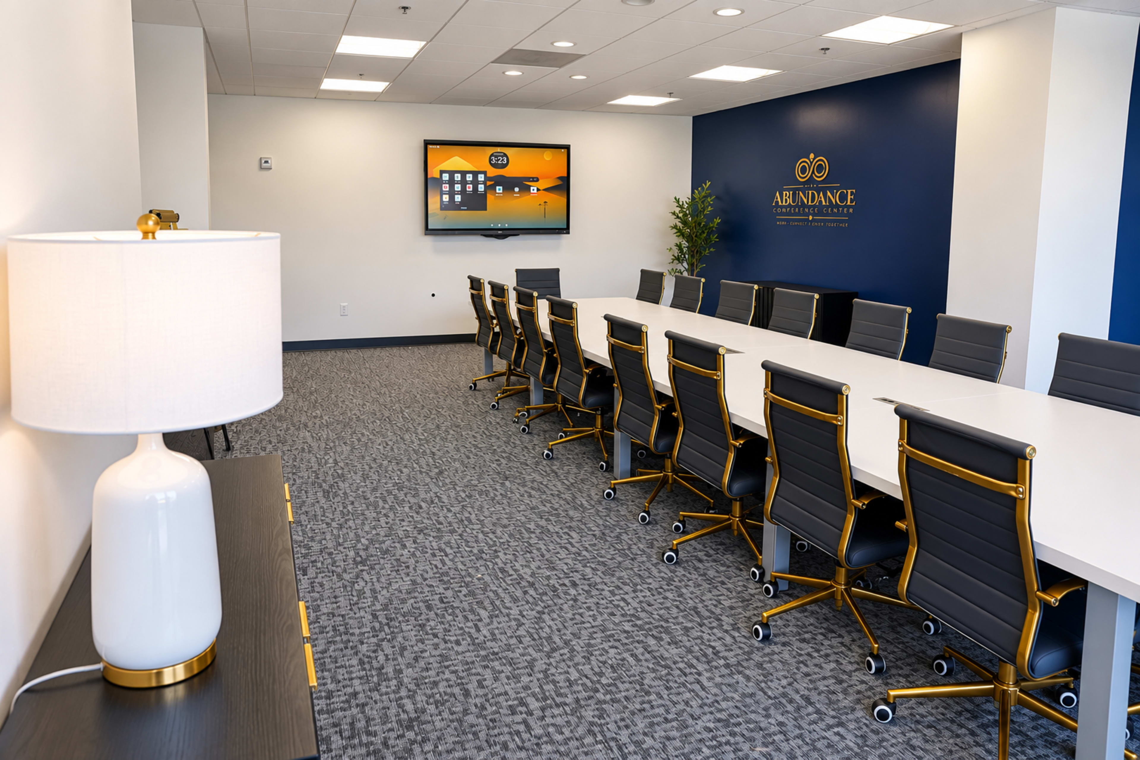 The image shows a modern conference room with a large white table, black rolling chairs, and a flat-screen TV mounted on a blue wall.