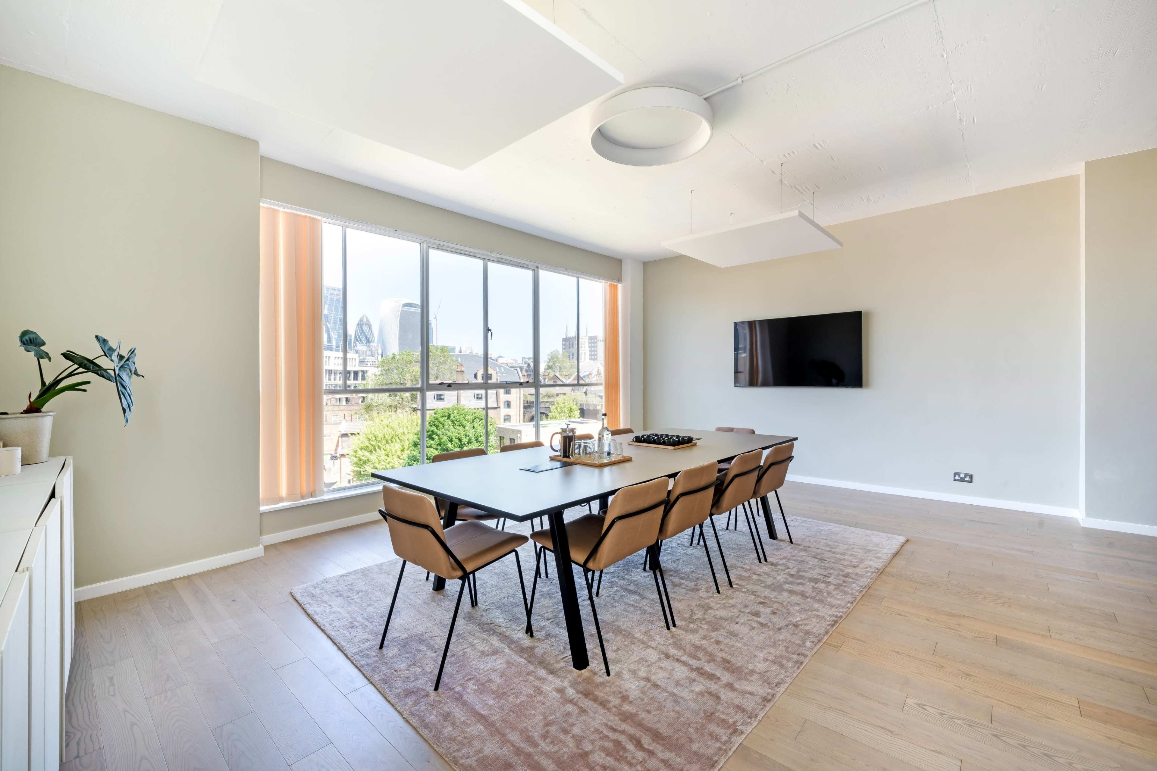 A modern conference room features a long table with eight chairs, large windows with city views, and a wall-mounted television.