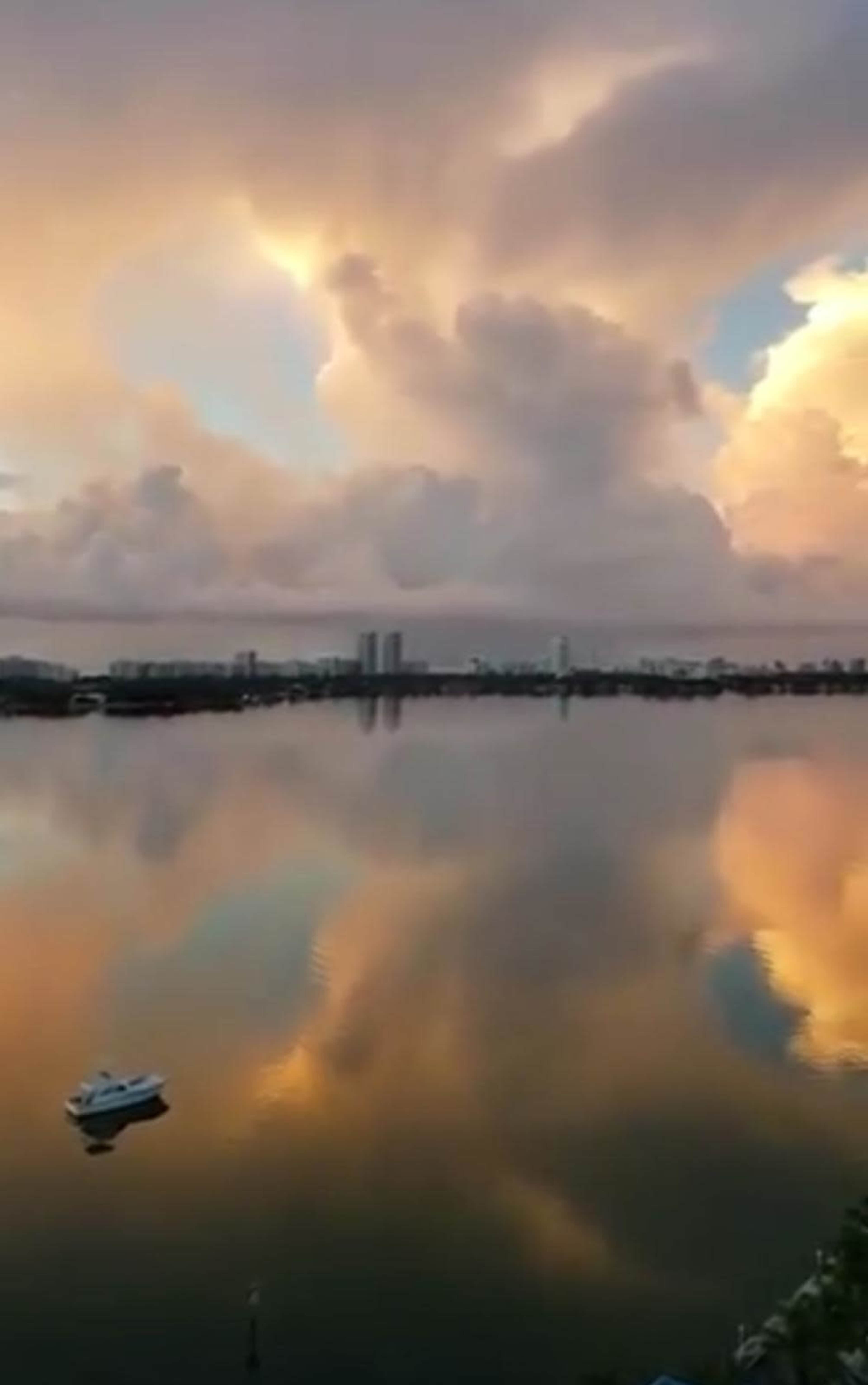 The image shows a serene body of water reflecting dramatic clouds at sunset, with a small boat anchored nearby.