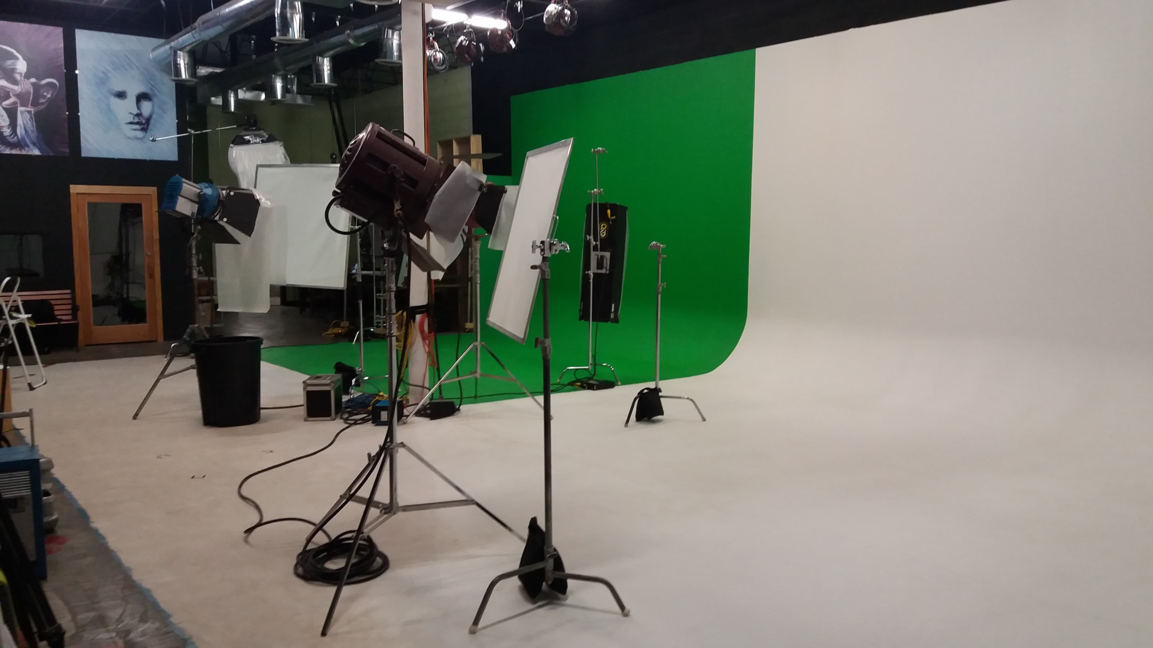 A photography studio equipped with lighting equipment, a green screen, and a white backdrop.