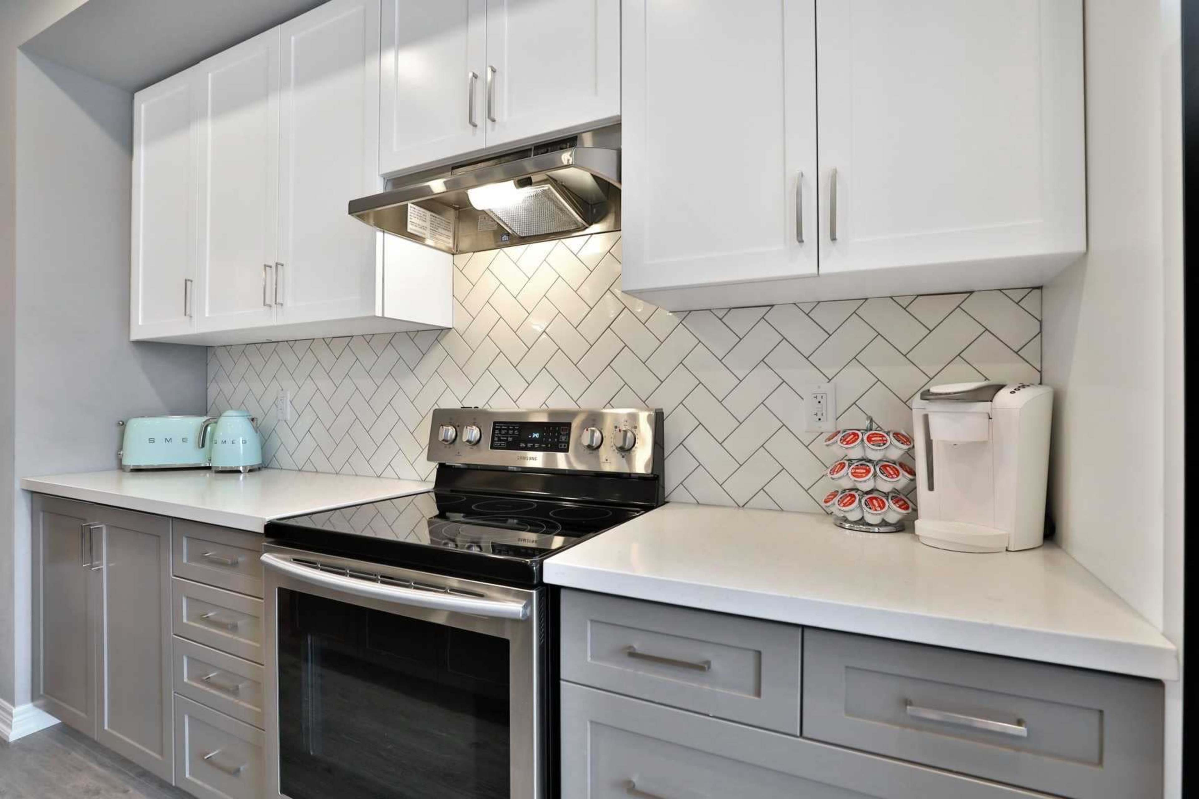 The image shows a modern kitchen featuring white cabinets, a stainless steel stove, and a herringbone-patterned backsplash.