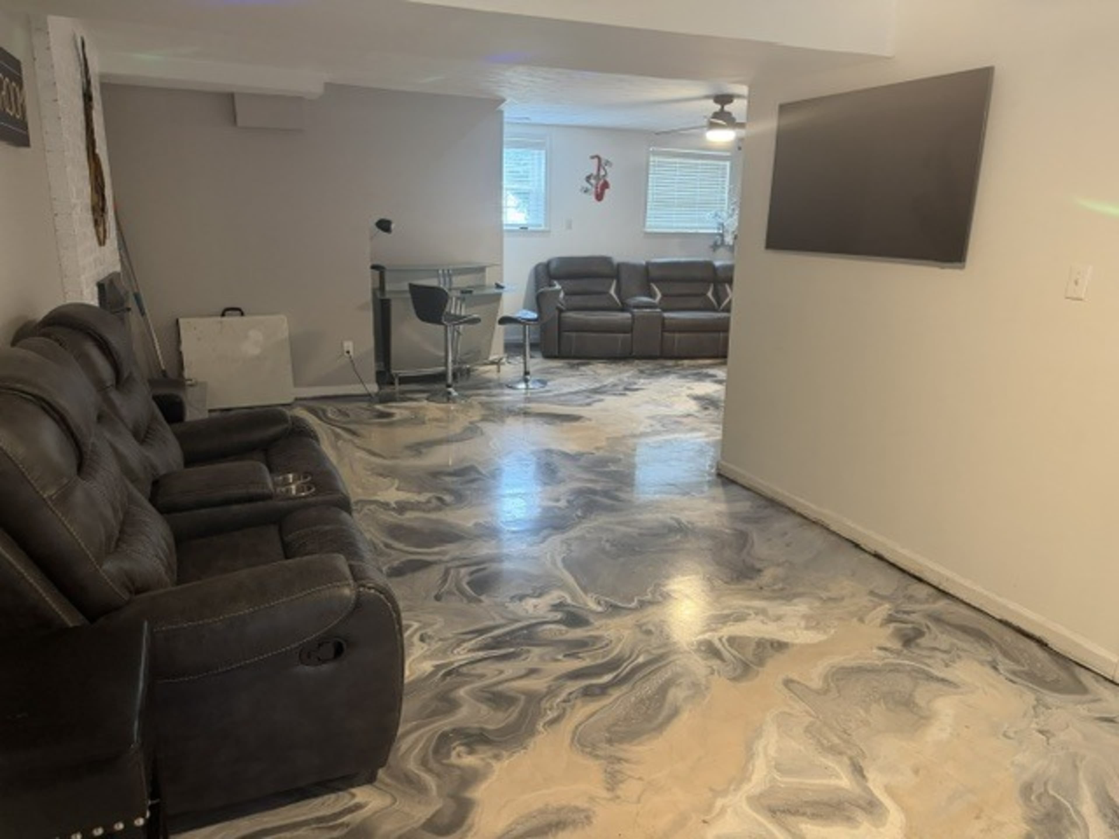 The image shows a modern living area featuring dark recliners, a glossy marbled floor, and a wall-mounted television.