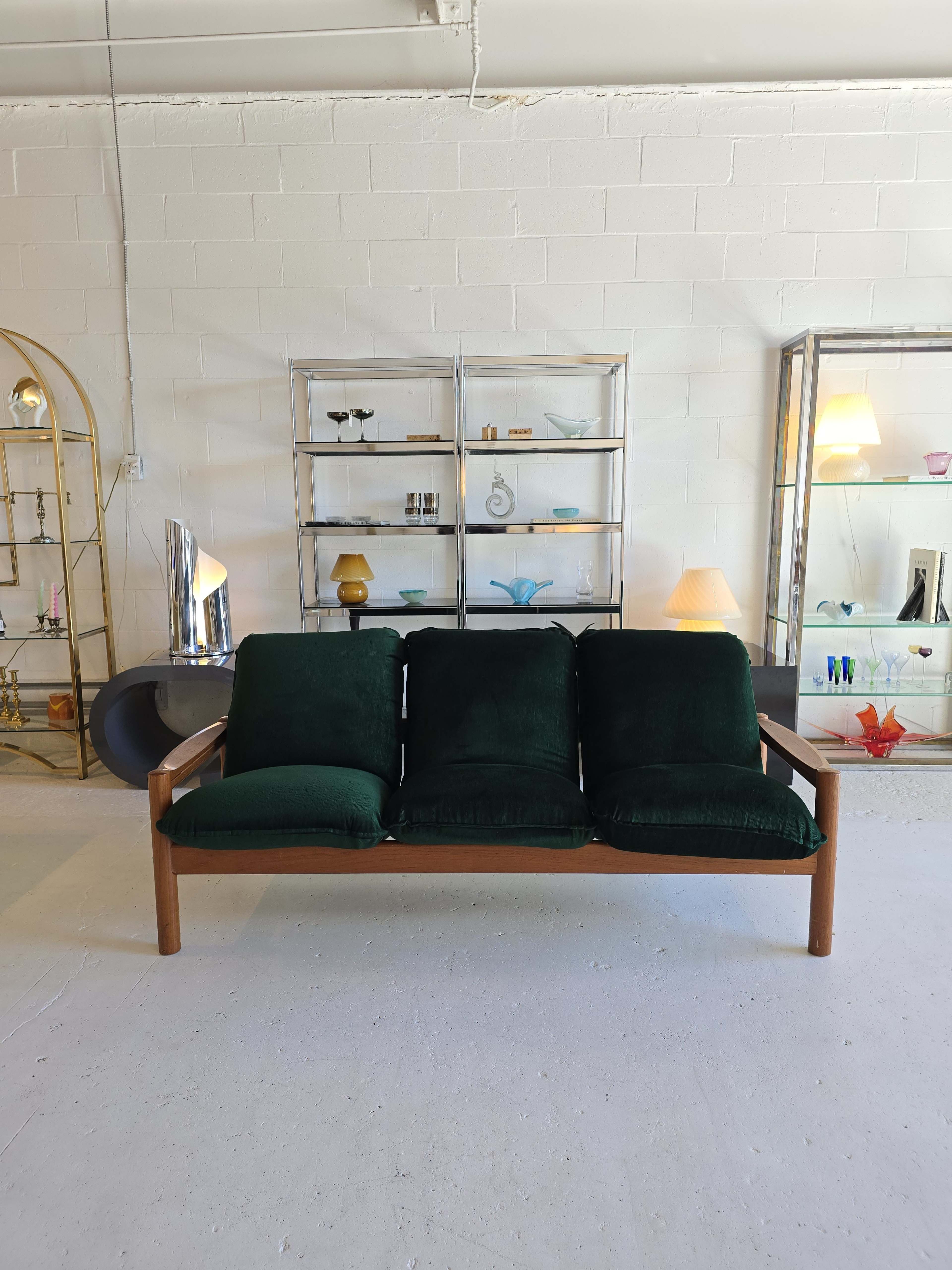 A green, upholstered three-seat sofa stands in front of a shelf displaying various decorative items and lamps.