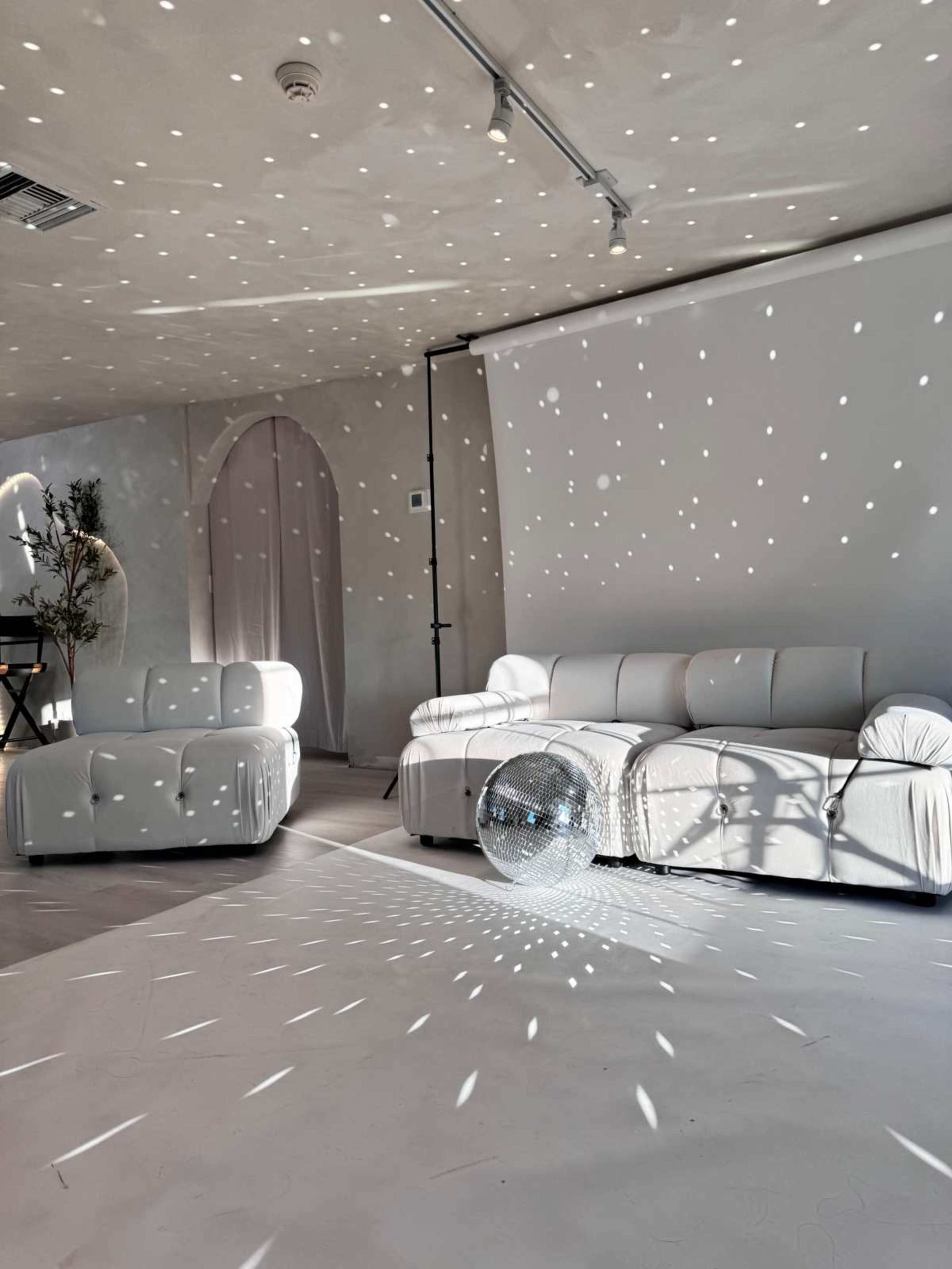 A minimalist room features white furniture and a disco ball casting light patterns on the floor and walls.
