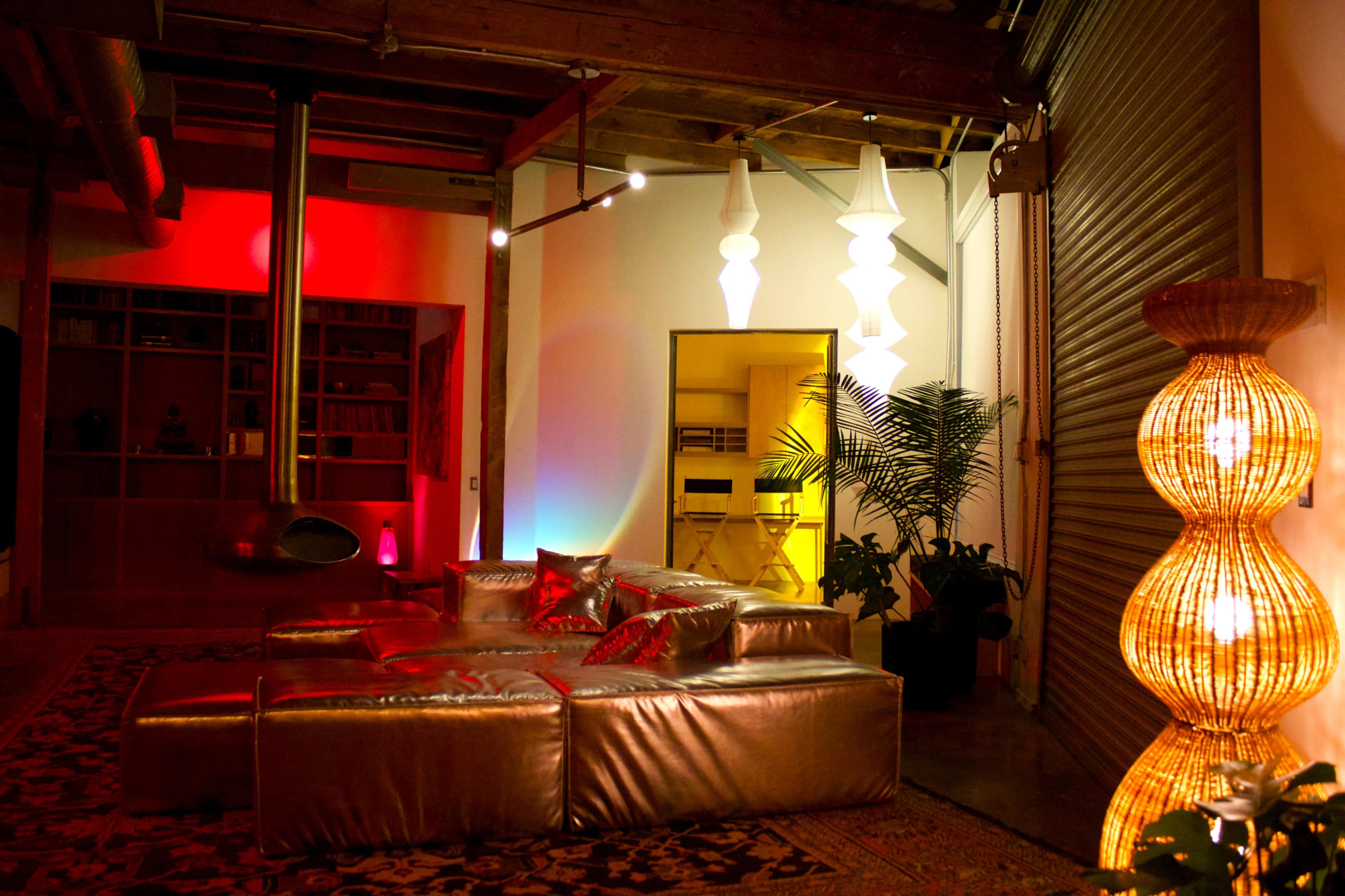 The image shows a modern living room with a metallic couch, colorful lighting, and a mix of plants and decorative lamps.