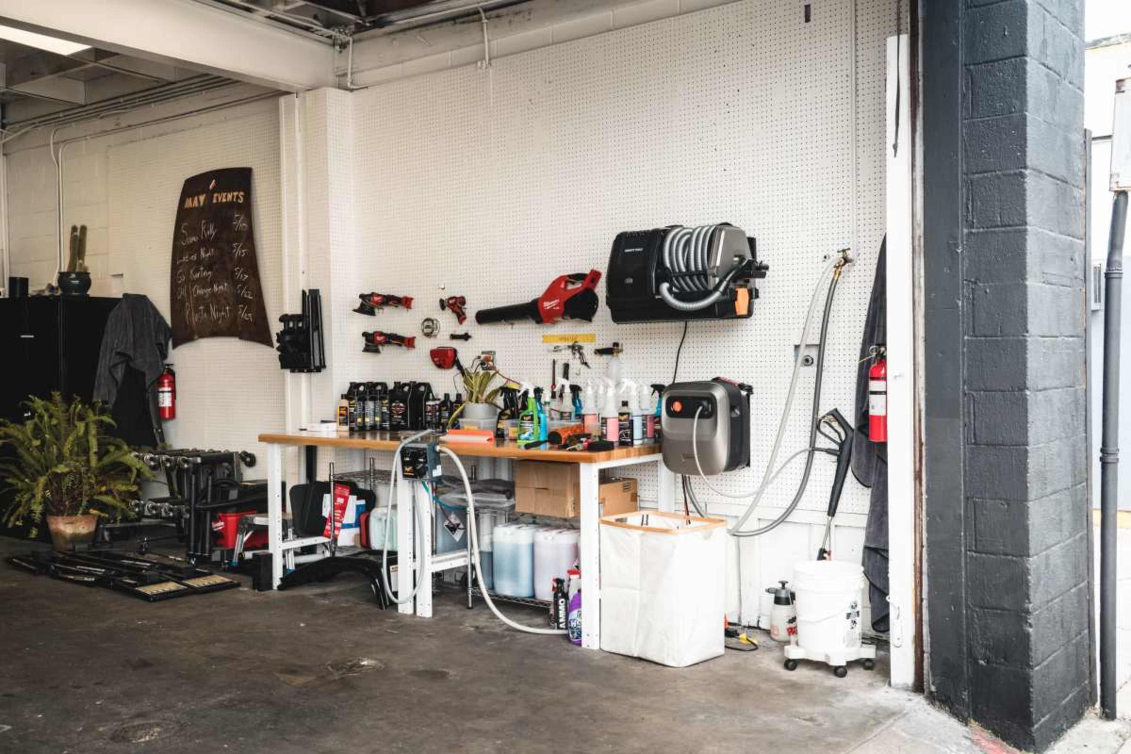 The image shows a workshop corner with a workbench, tools mounted on a pegboard, and various containers and equipment for maintenance tasks.