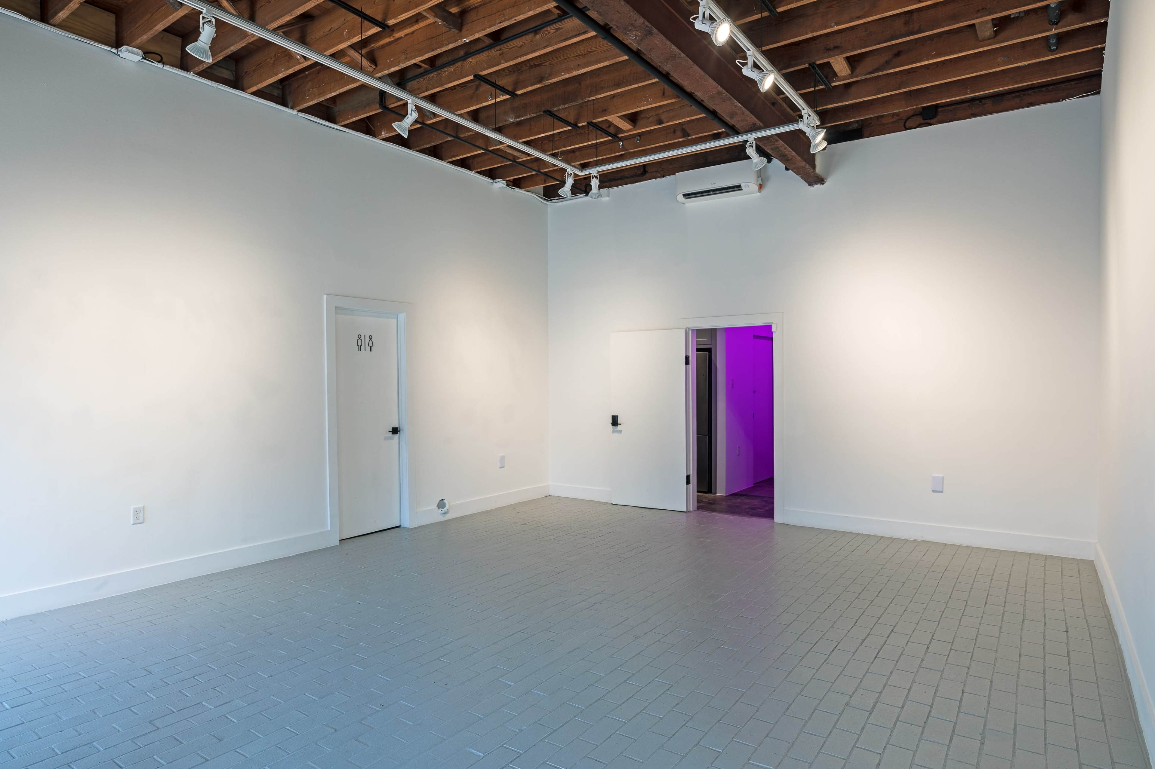 A sparse art gallery features a plain white interior with a door on one side and a purple-lit entrance on the other.