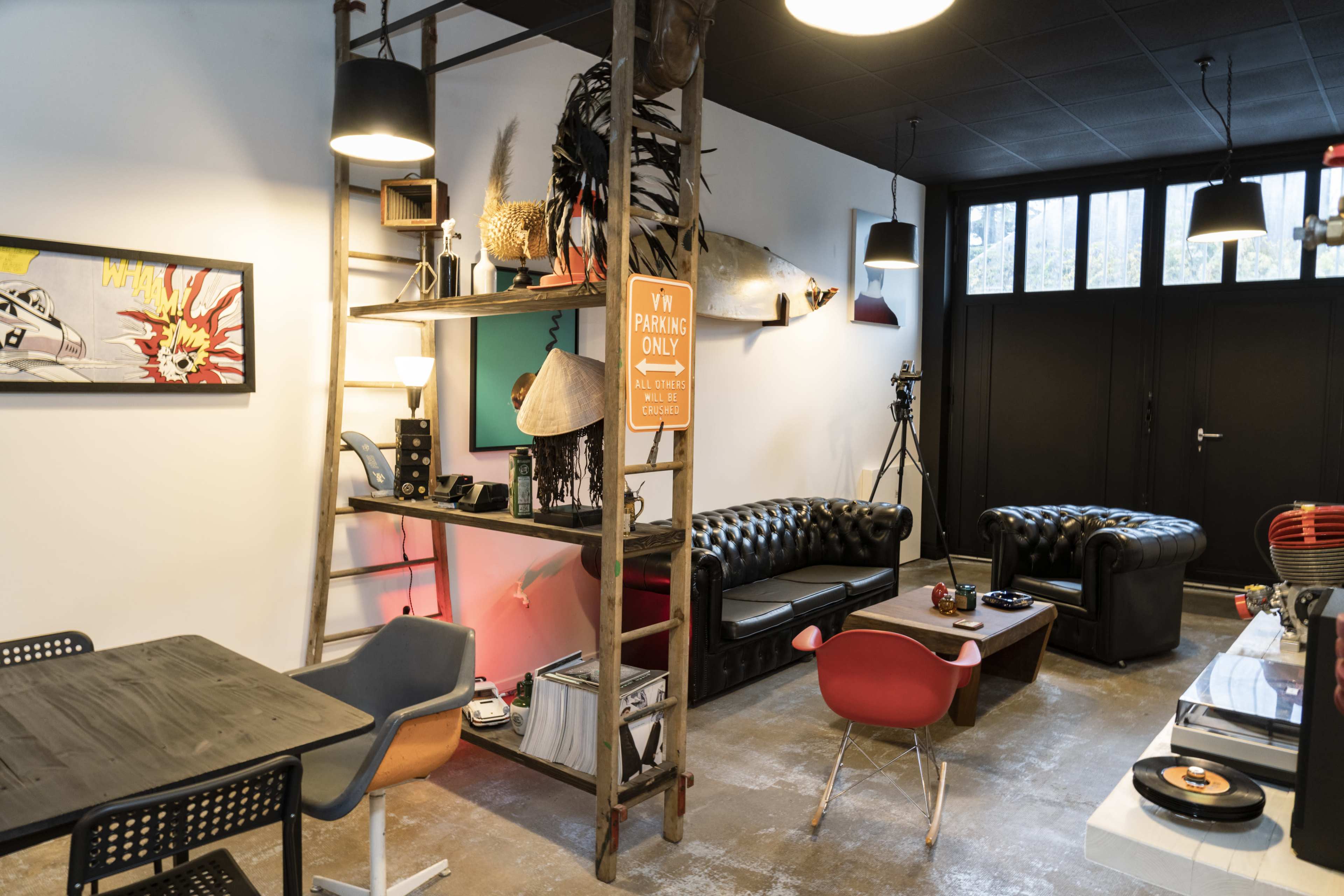 A modern interior space featuring black leather sofas, a wooden table with chairs, and shelves displaying various decor items and a vintage sign.