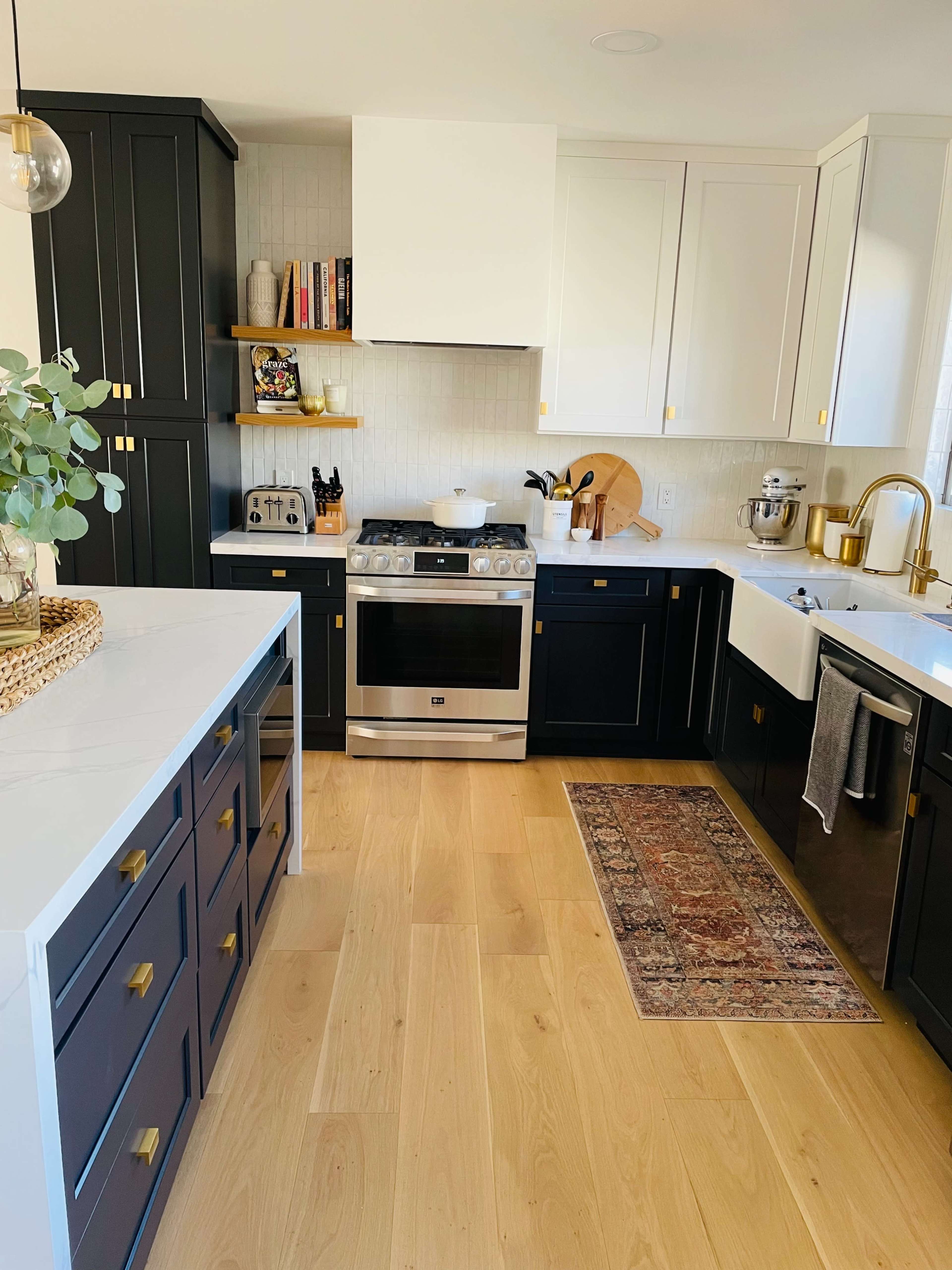 A modern kitchen with black and white cabinetry, a stainless steel stove, and a wooden floor, accented by a decorative rug.