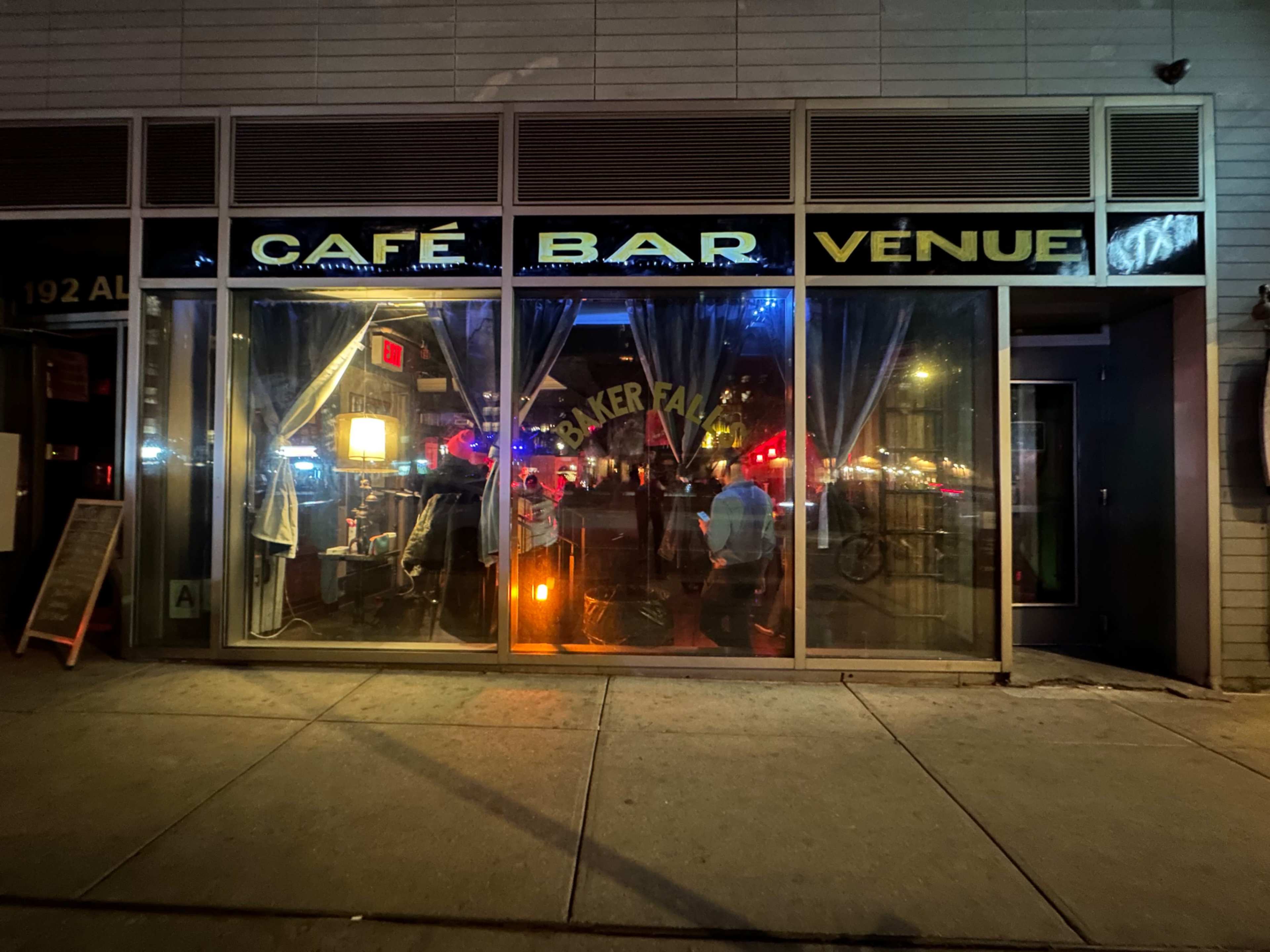 The image shows a café bar venue with large glass windows, where the interior is dimly lit and decorated with colorful lights.