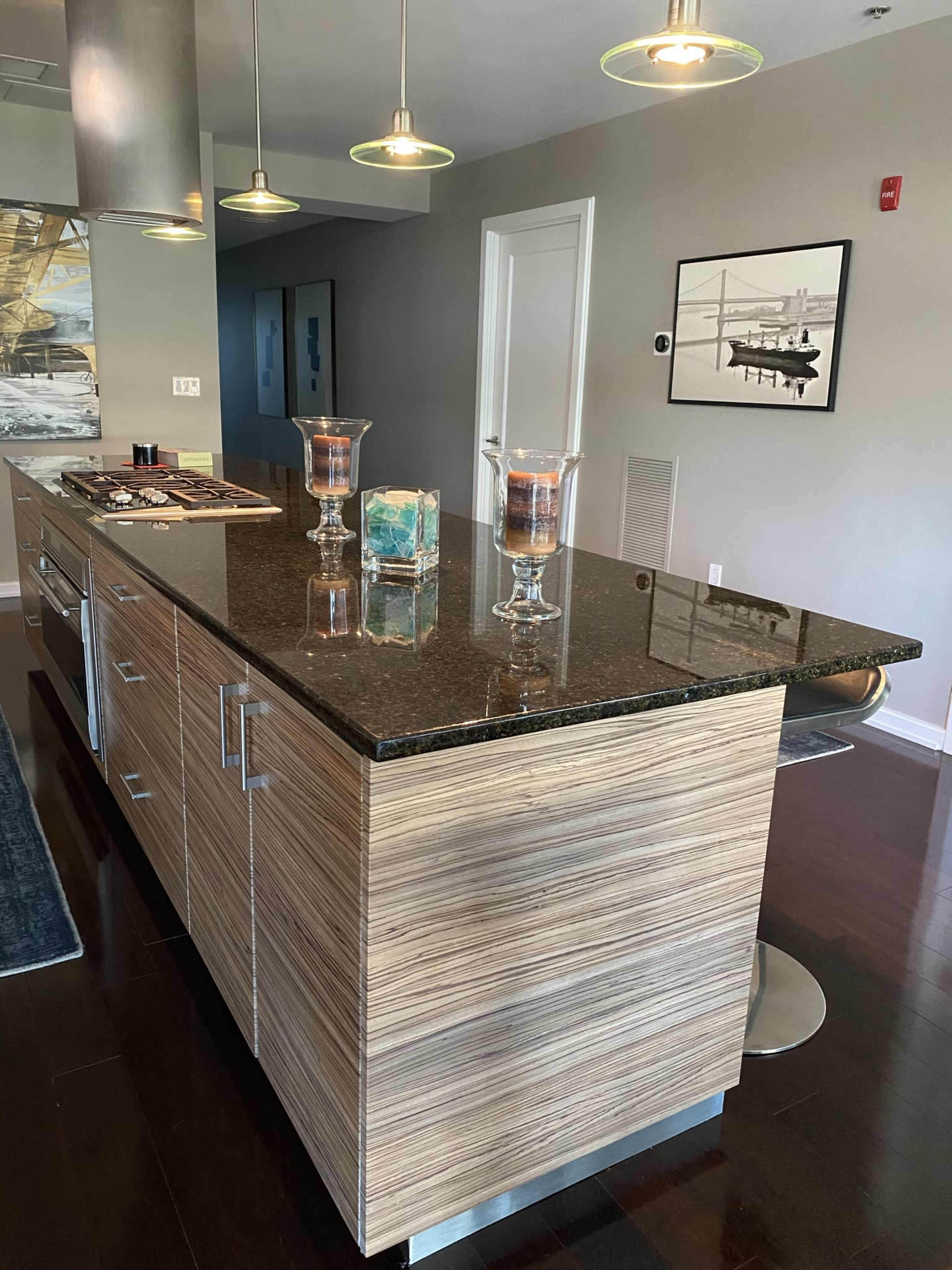 A modern kitchen island with a dark granite countertop and a wooden base, featuring decorative candles and a glass art piece on top.