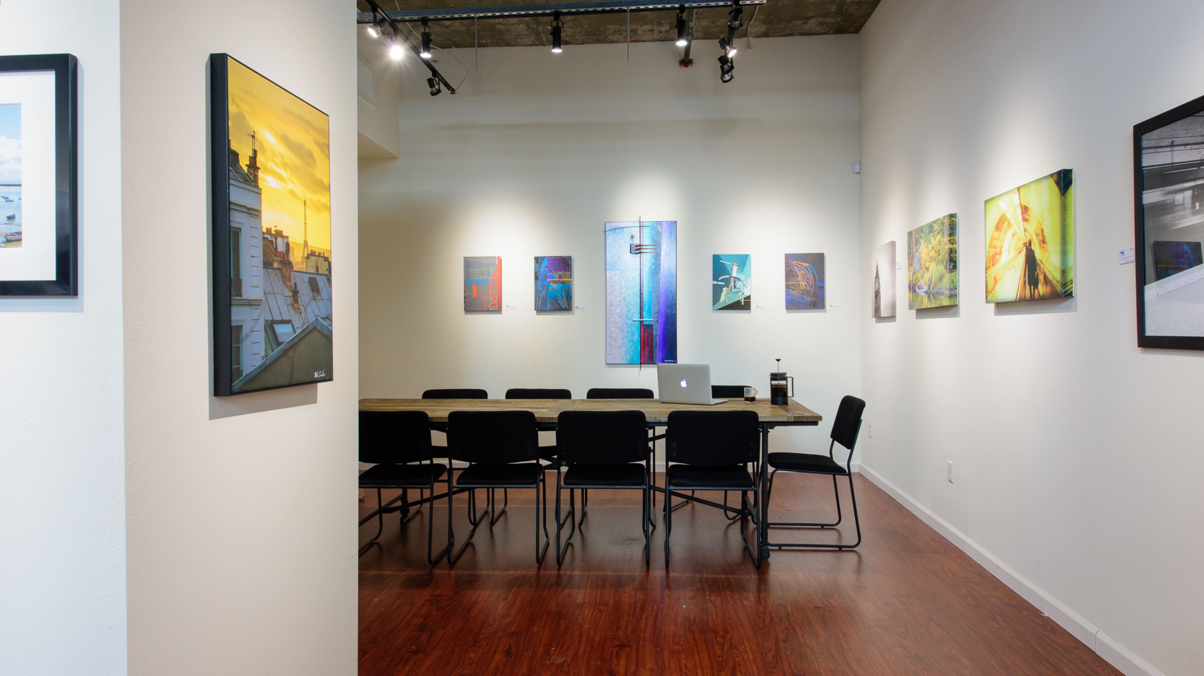 A modern meeting room features a long wooden table surrounded by black chairs, with colorful artwork displayed on the walls.