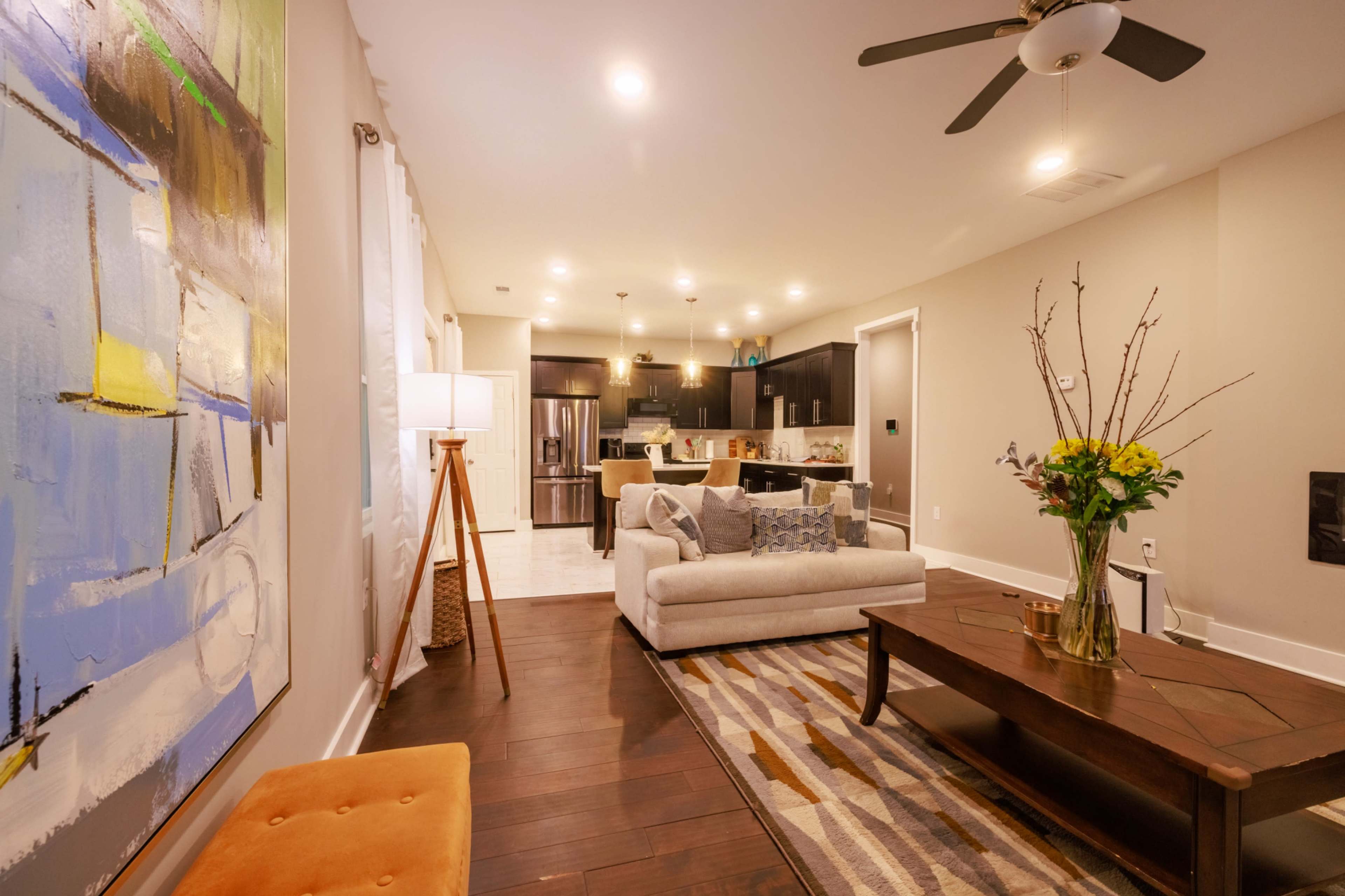 A modern living room with a gray sofa, a coffee table, a decorative floor lamp, and a kitchen visible in the background.
