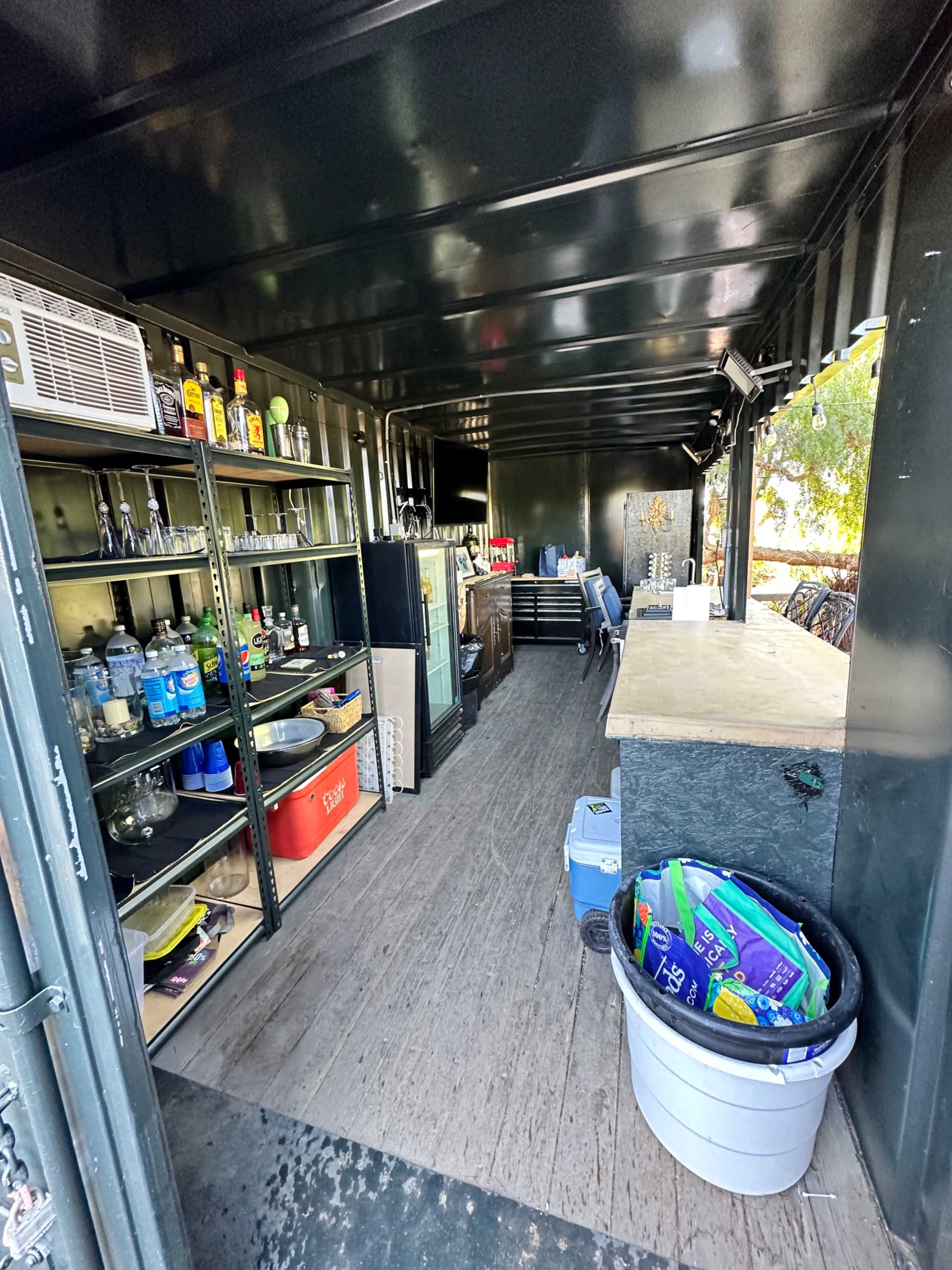 The interior of a storage container that is organized with shelves holding various bottles and equipment, alongside a countertop and other items.
