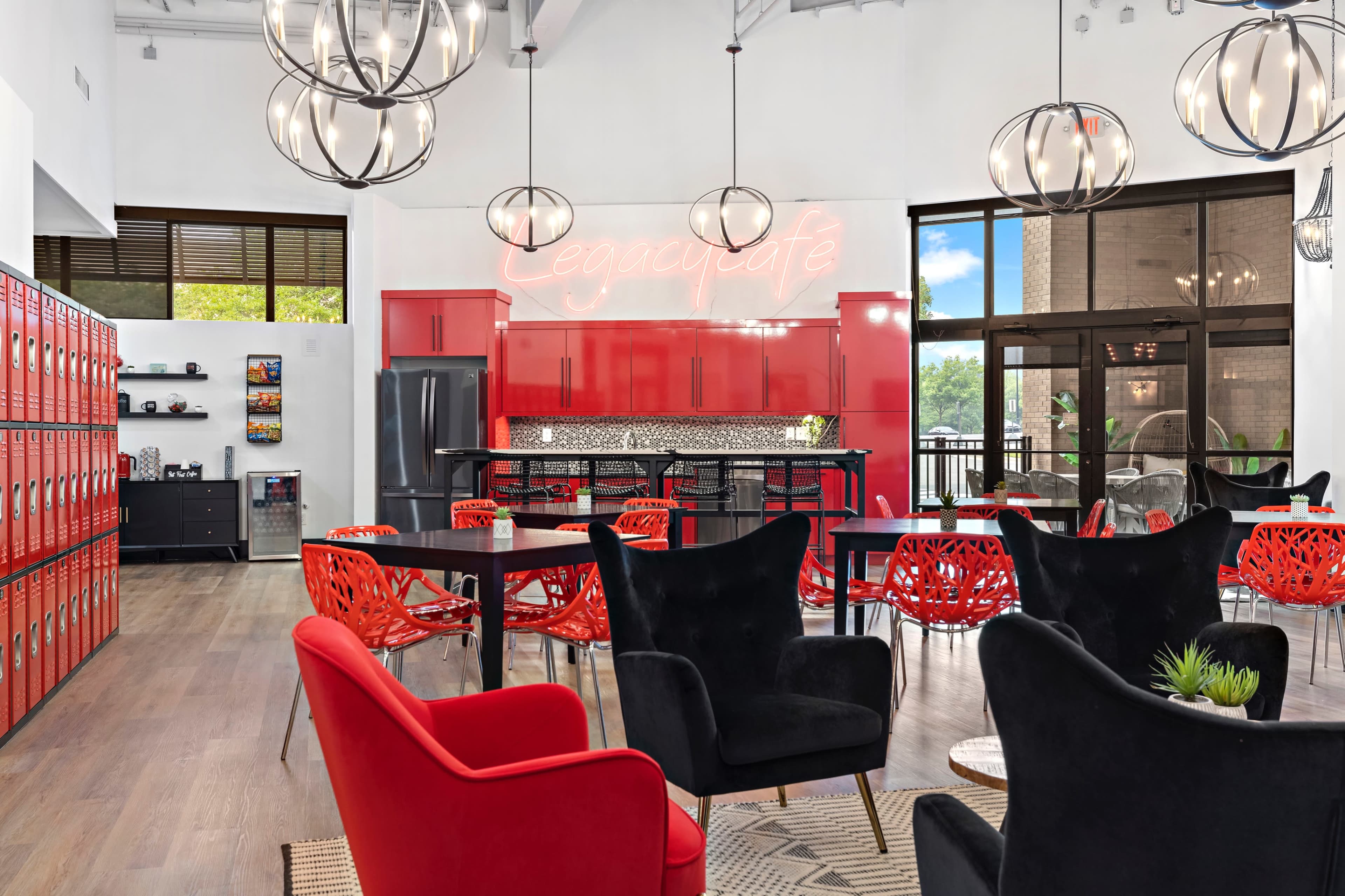 A modern common area with red lockers, a kitchenette, black and red seating, and large light fixtures.