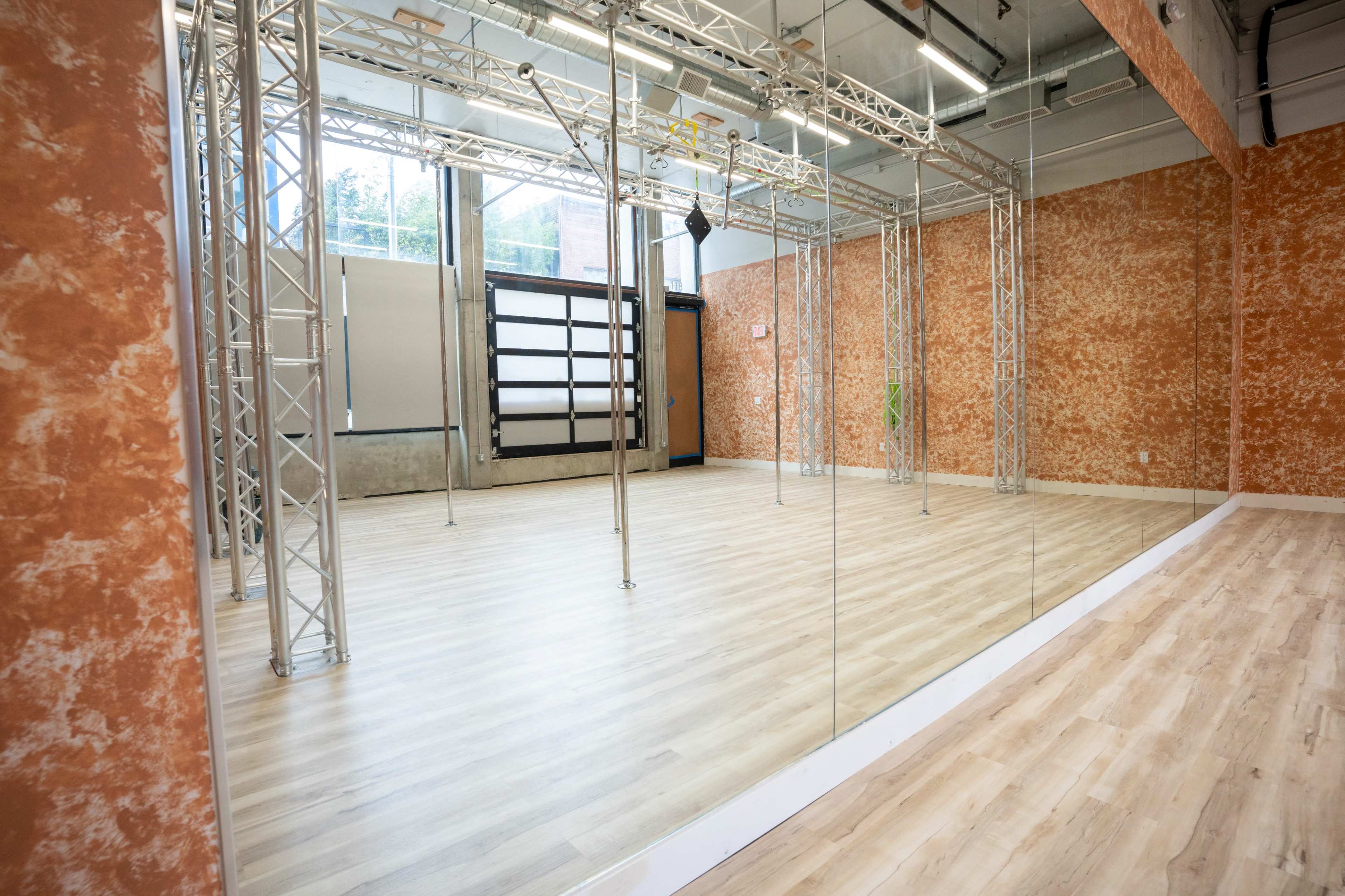 A spacious studio with a polished wooden floor, large mirrors on one wall, and metal support structures in the center.
