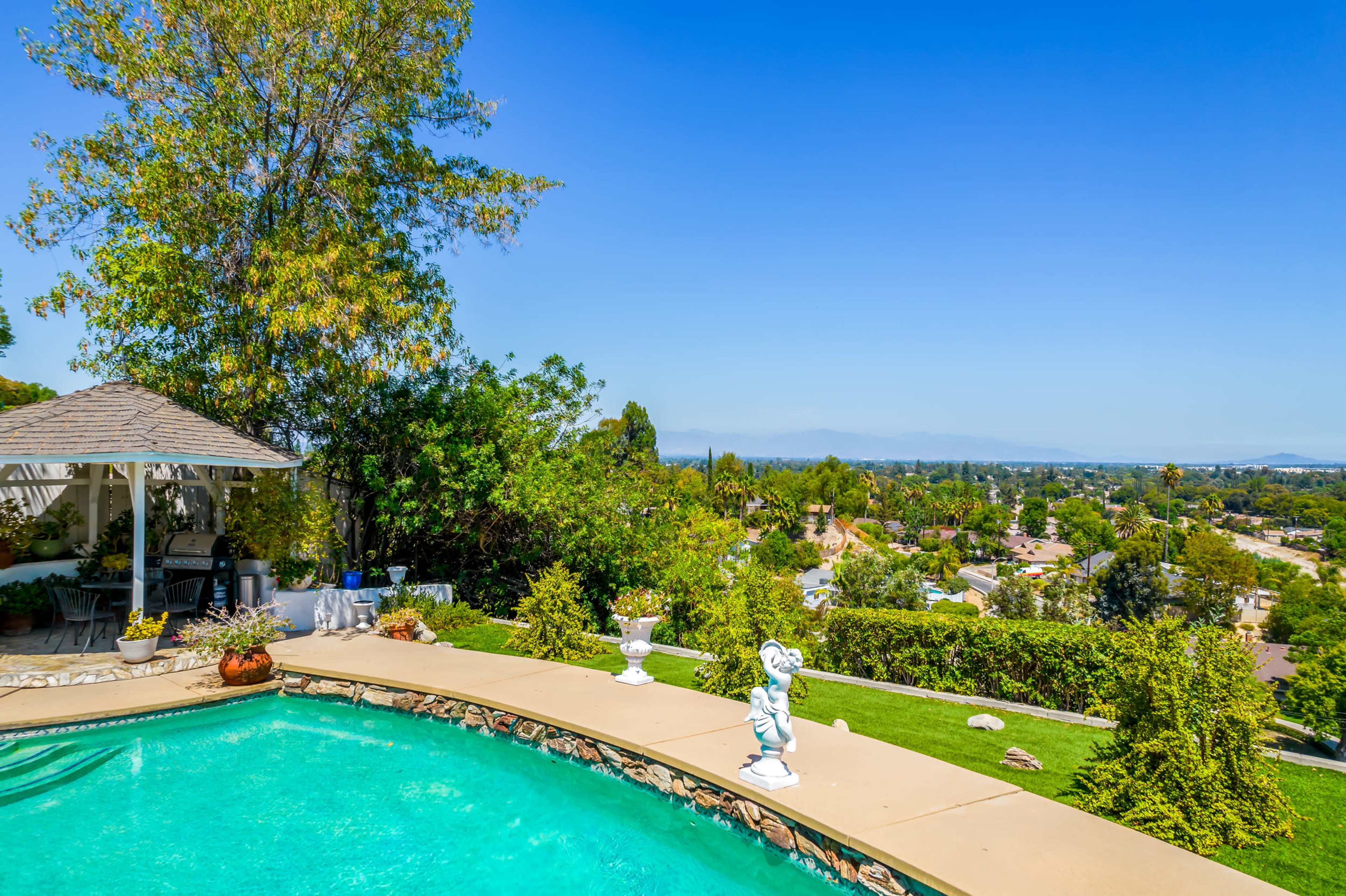 A swimming pool with a decorative statue overlooks a residential area and distant mountains under a clear blue sky.