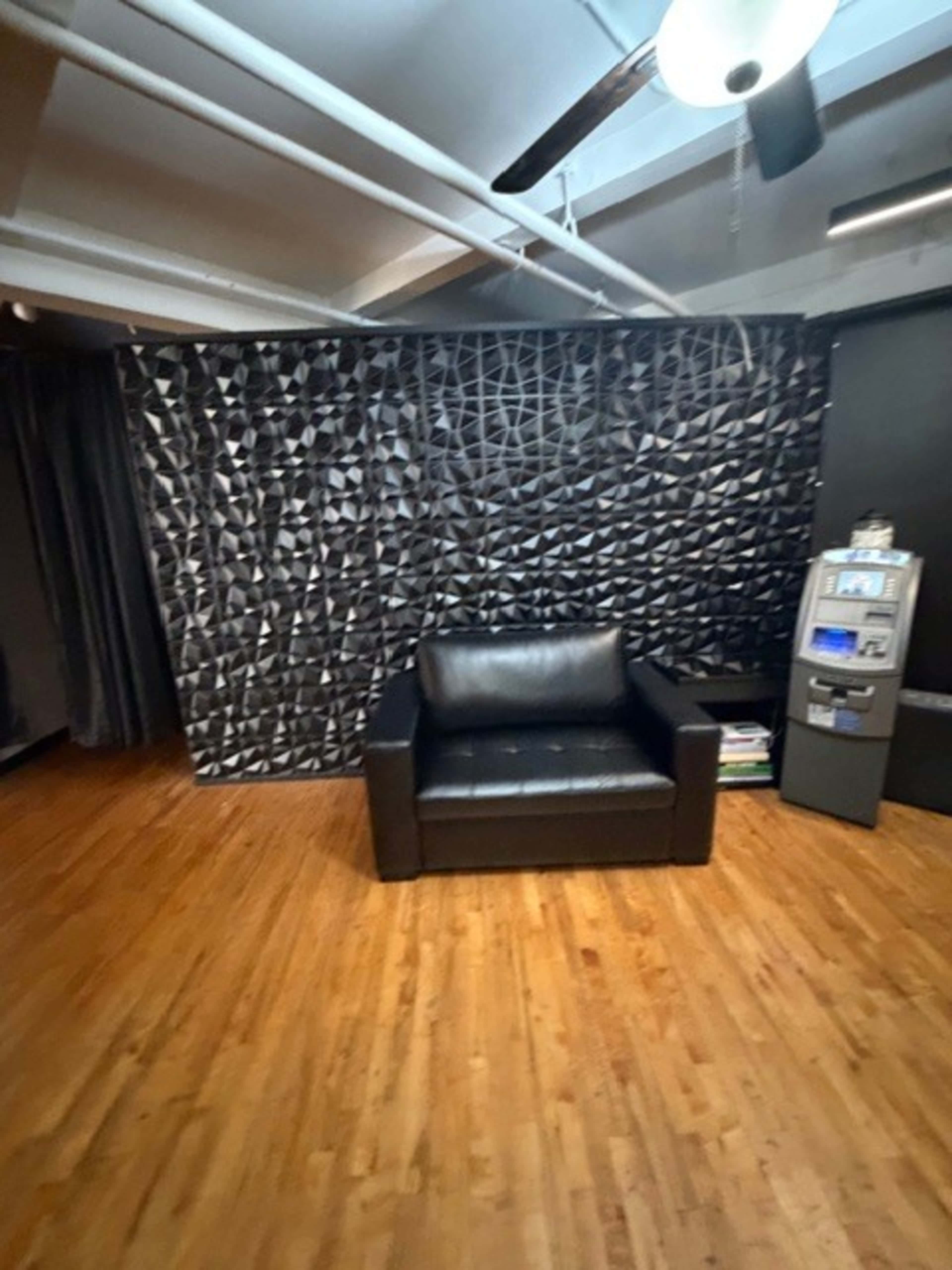 The image shows a small room with a black leather armchair, a textured black wall, and a display unit against the wall.