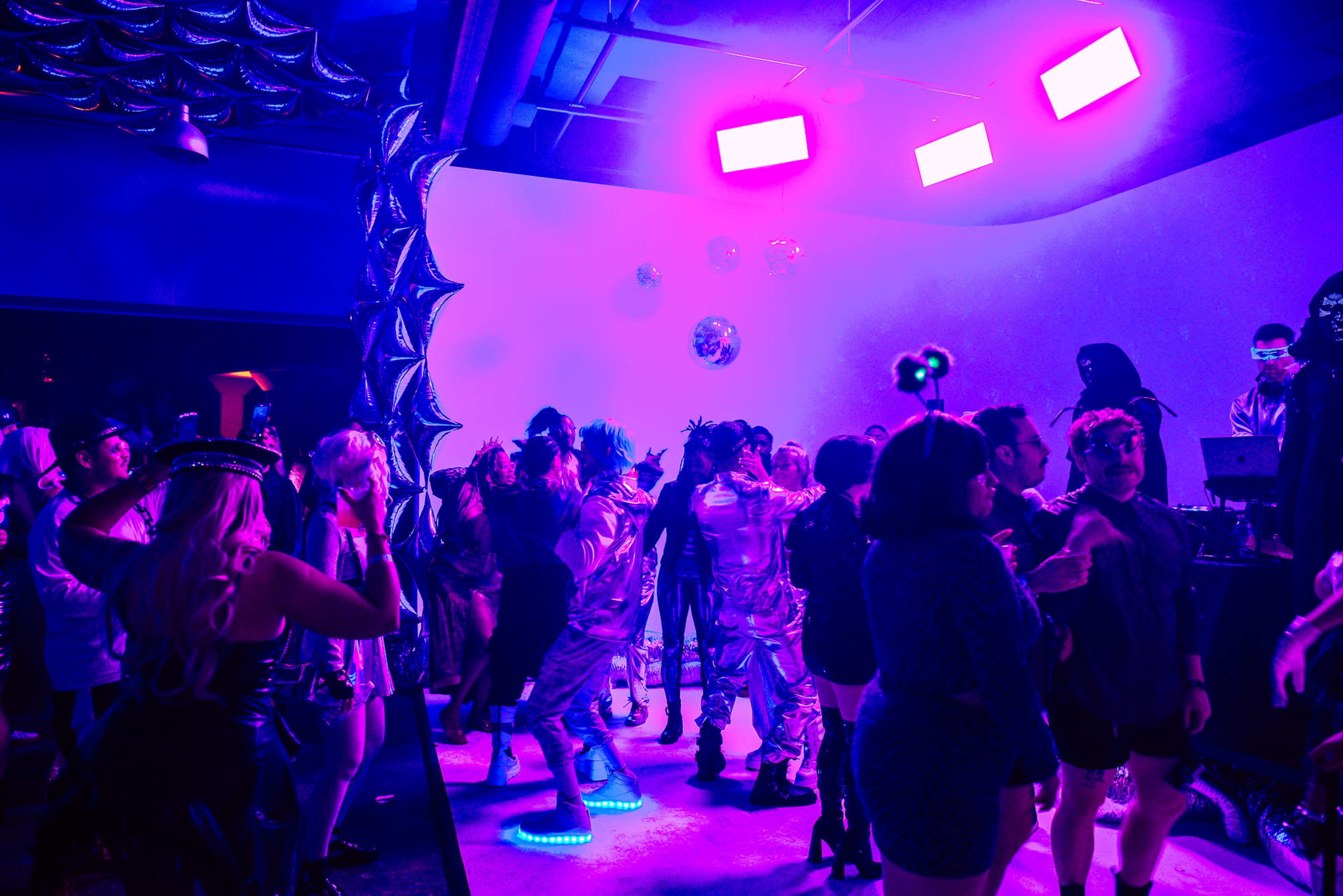 A crowd dances under colorful lights in a vibrant party scene.