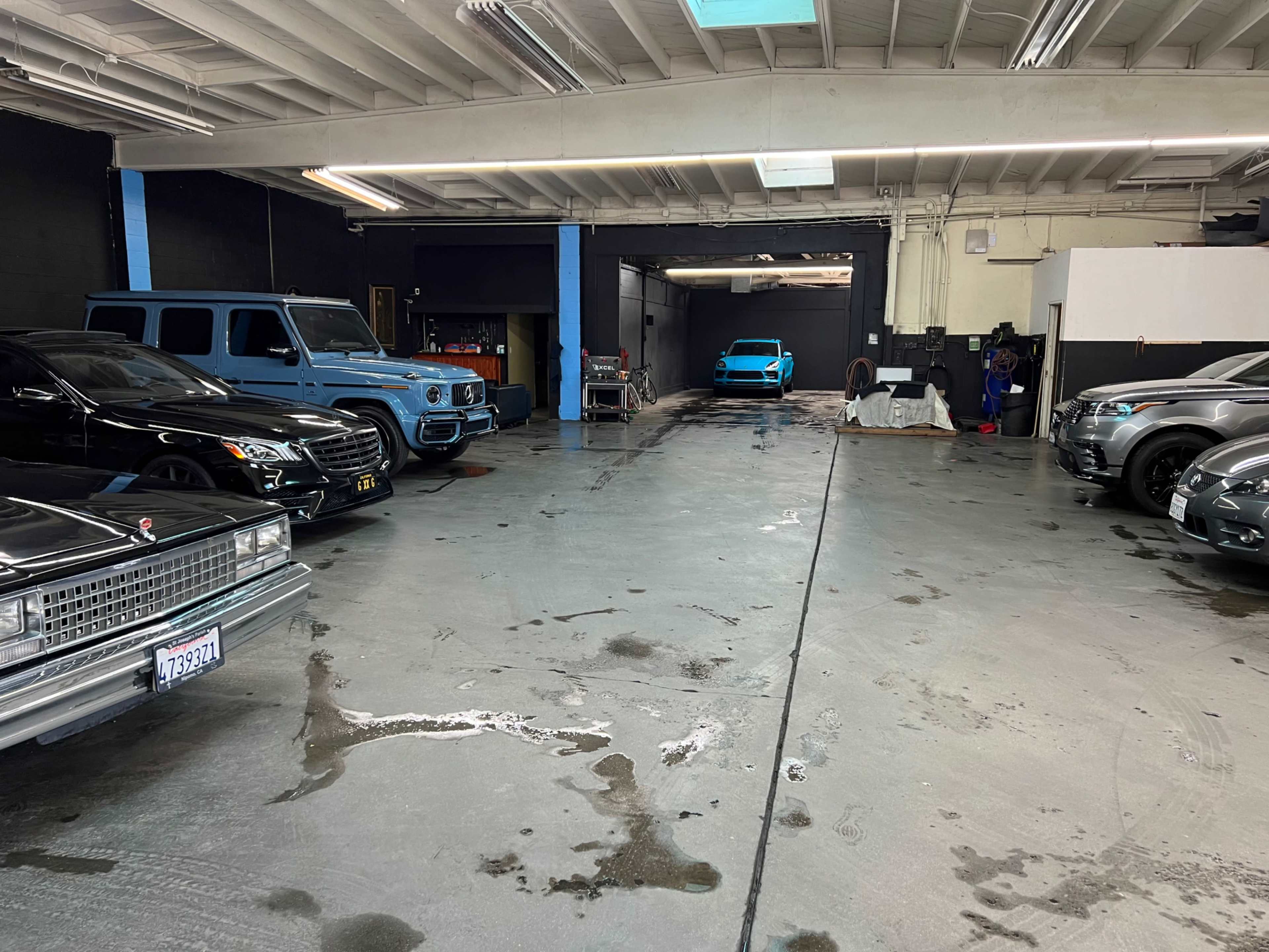 The image shows a spacious garage with several luxury vehicles, including a black SUV, a vintage car, and a blue sports car, arranged in an orderly manner.