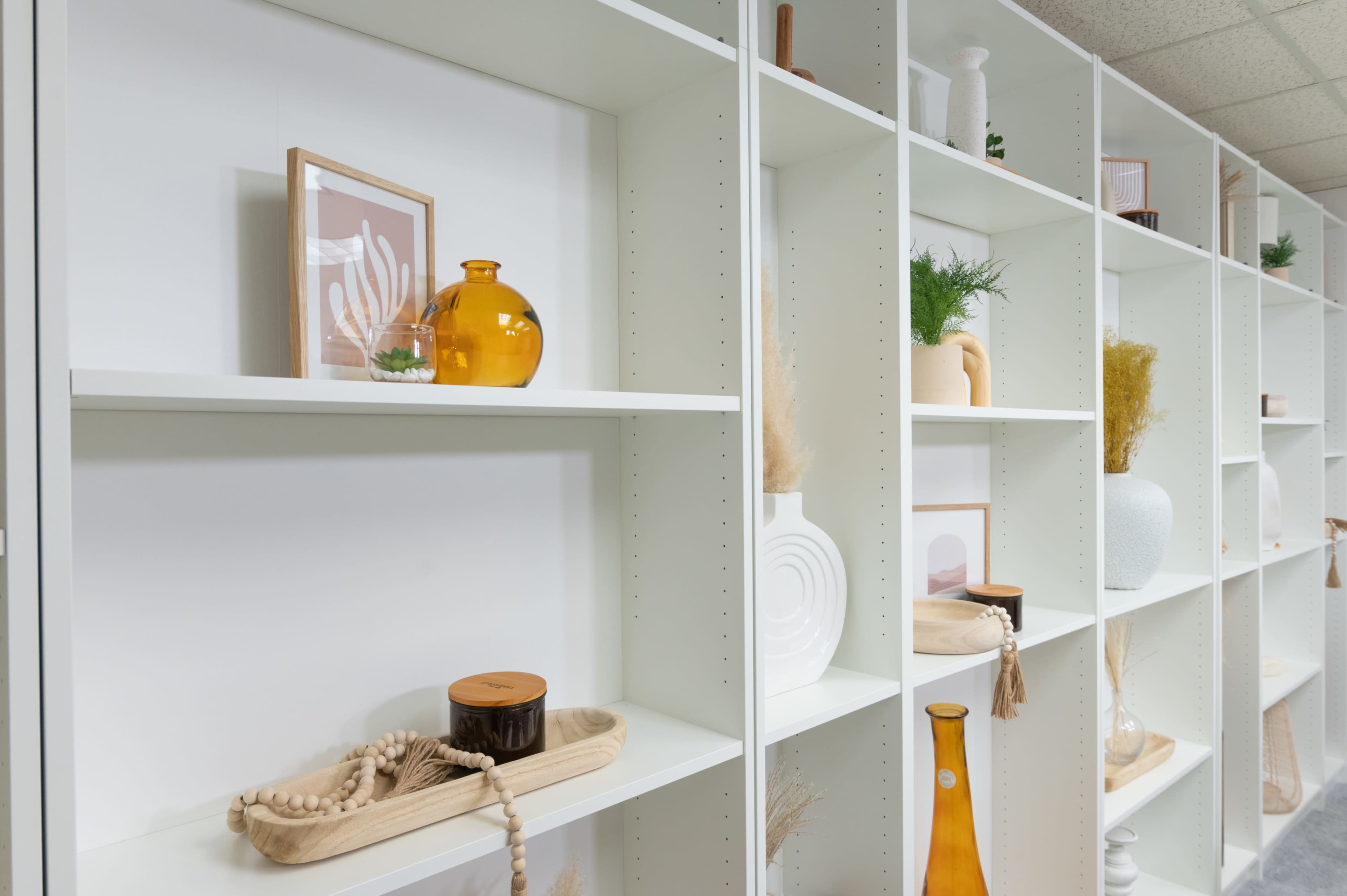 A white shelving unit displays various decorative items, including vases, framed artwork, and natural elements.