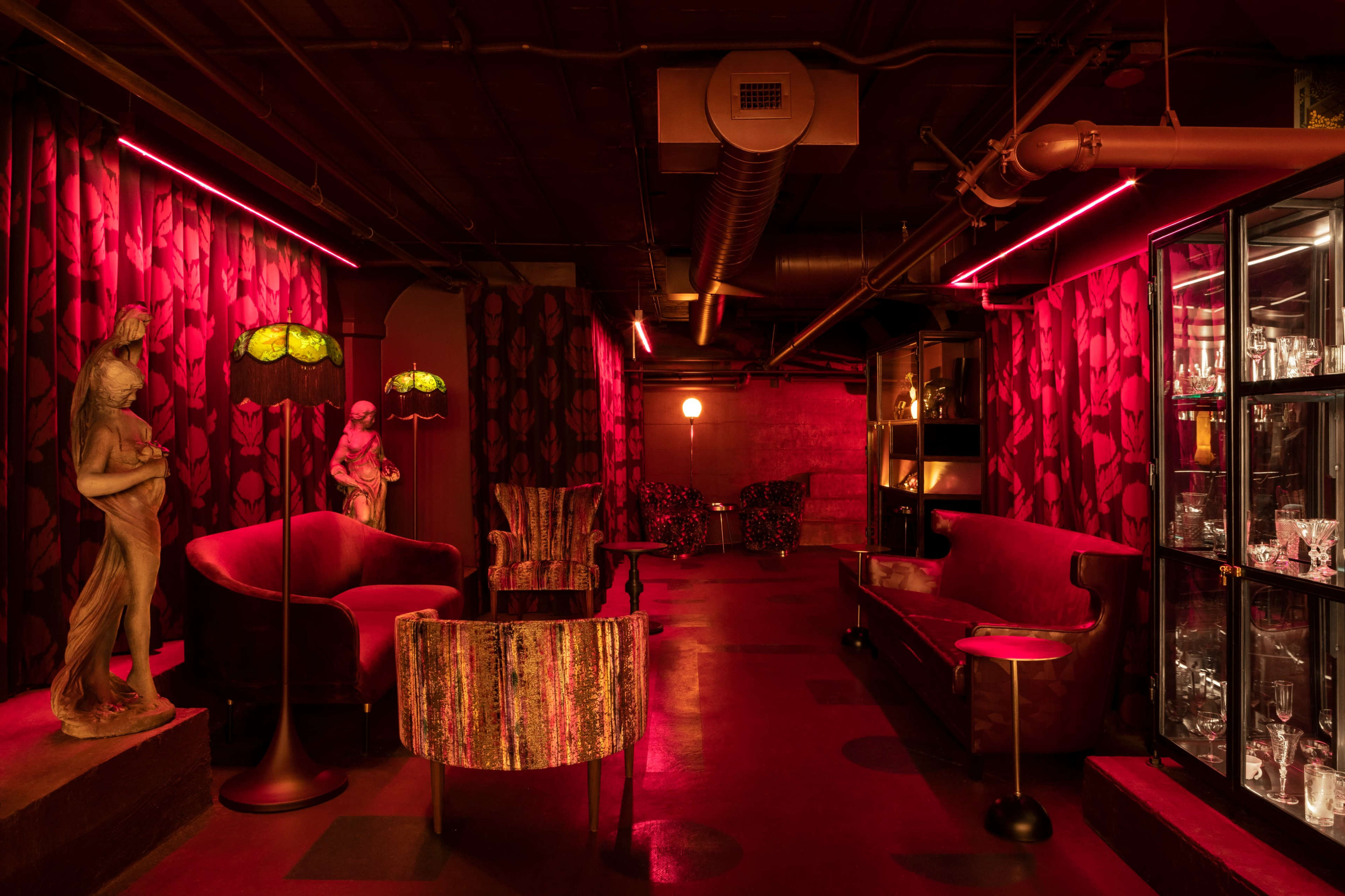 The scene features a dimly lit lounge area with red lighting, showcasing vintage furniture, decorative statues, and a glass display cabinet.