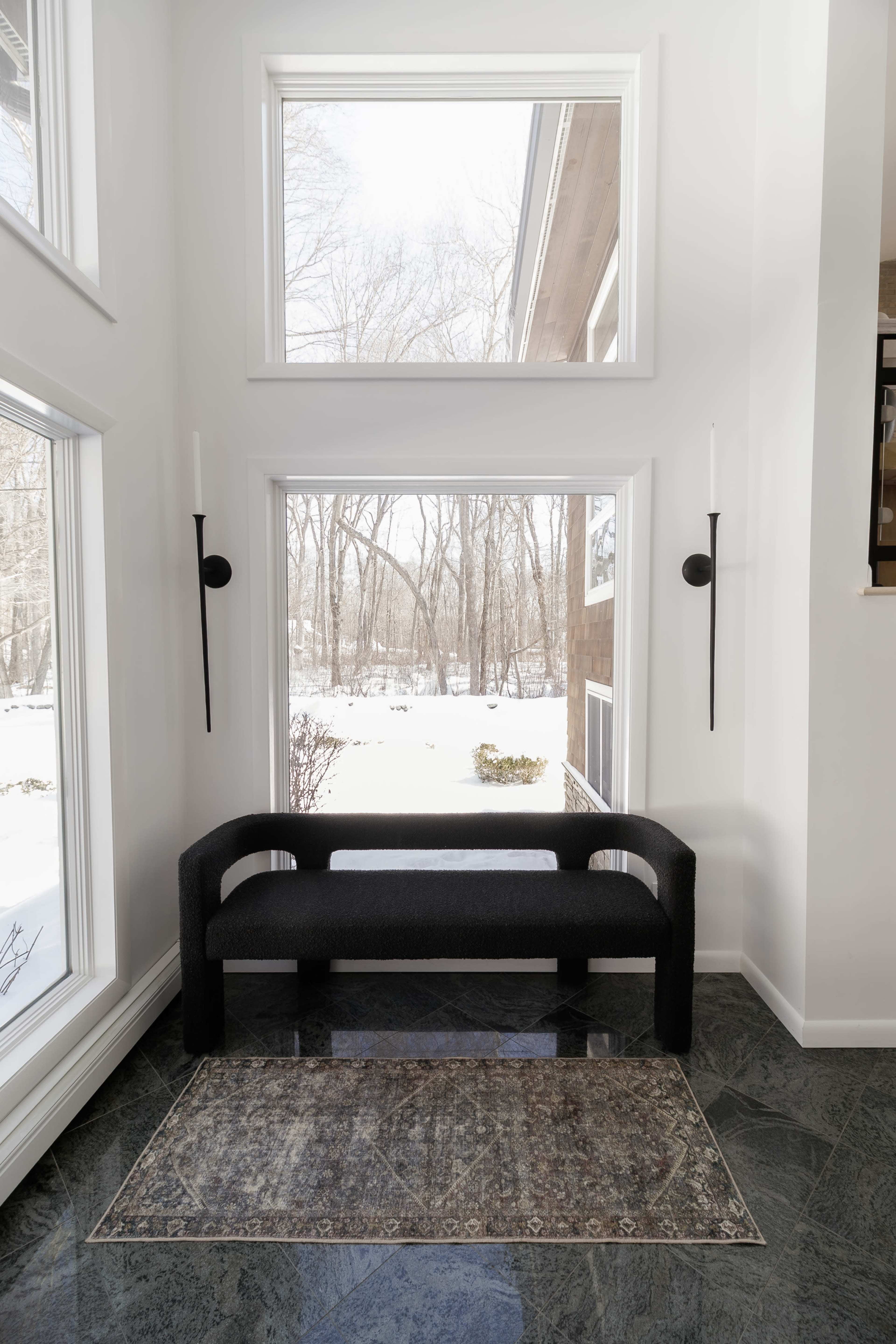 A modern black bench is positioned in front of large windows overlooking a snowy outdoor landscape.