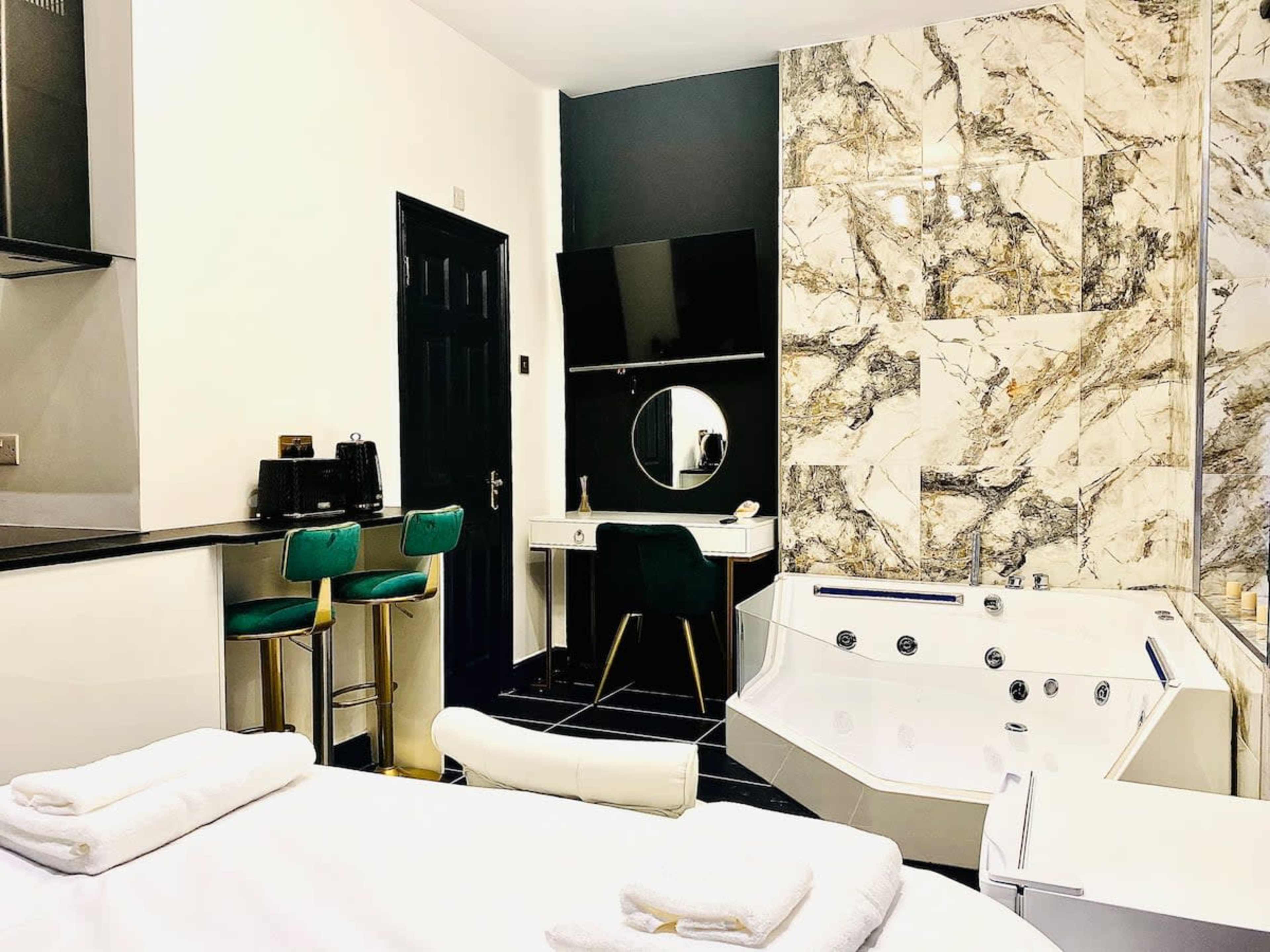 A modern bathroom featuring a large jacuzzi tub, a sleek vanity with a round mirror, and a small kitchenette area with bar stools.