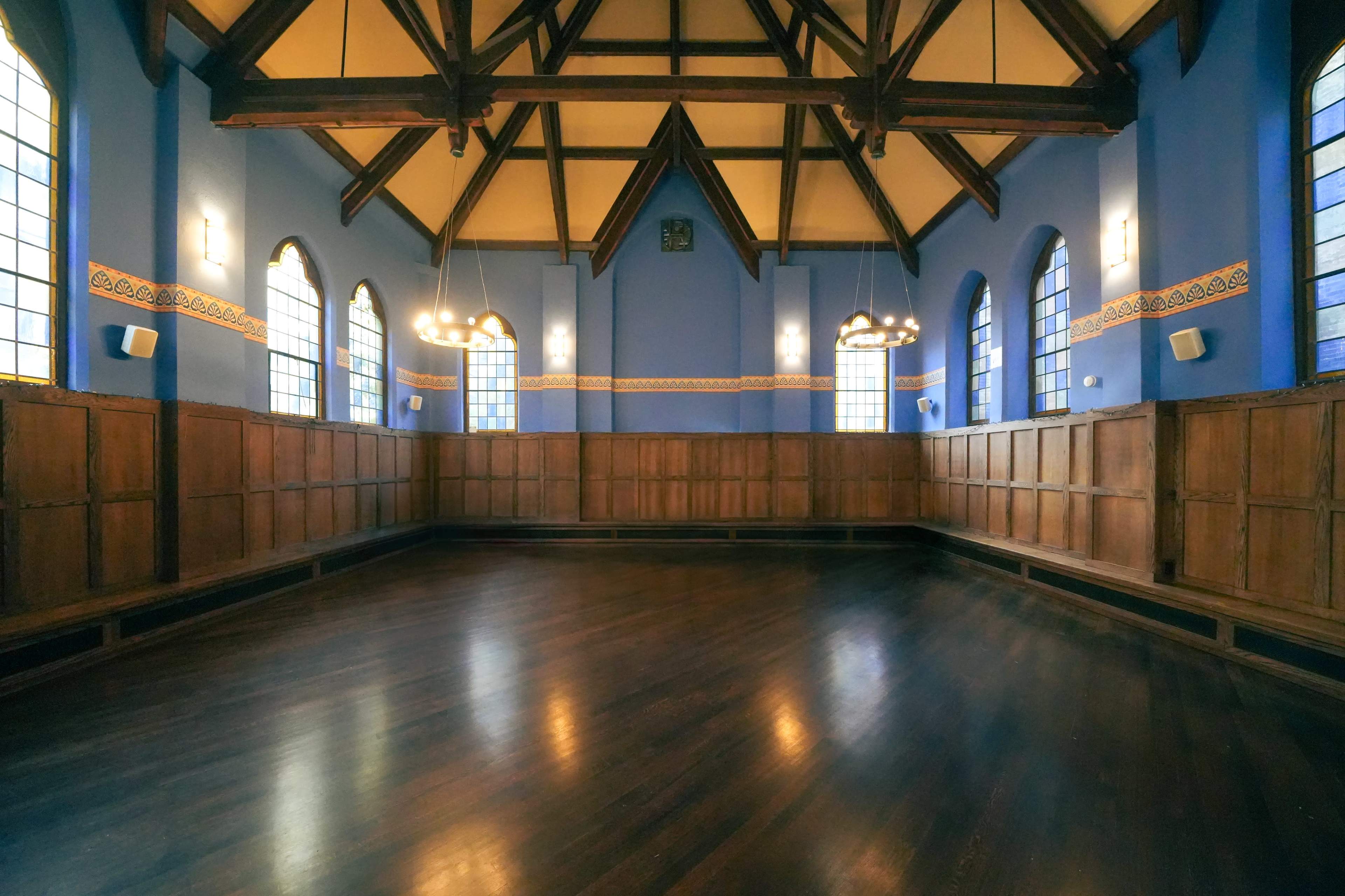A spacious room with wooden paneling, tall arched windows, and a vaulted ceiling supported by exposed beams.