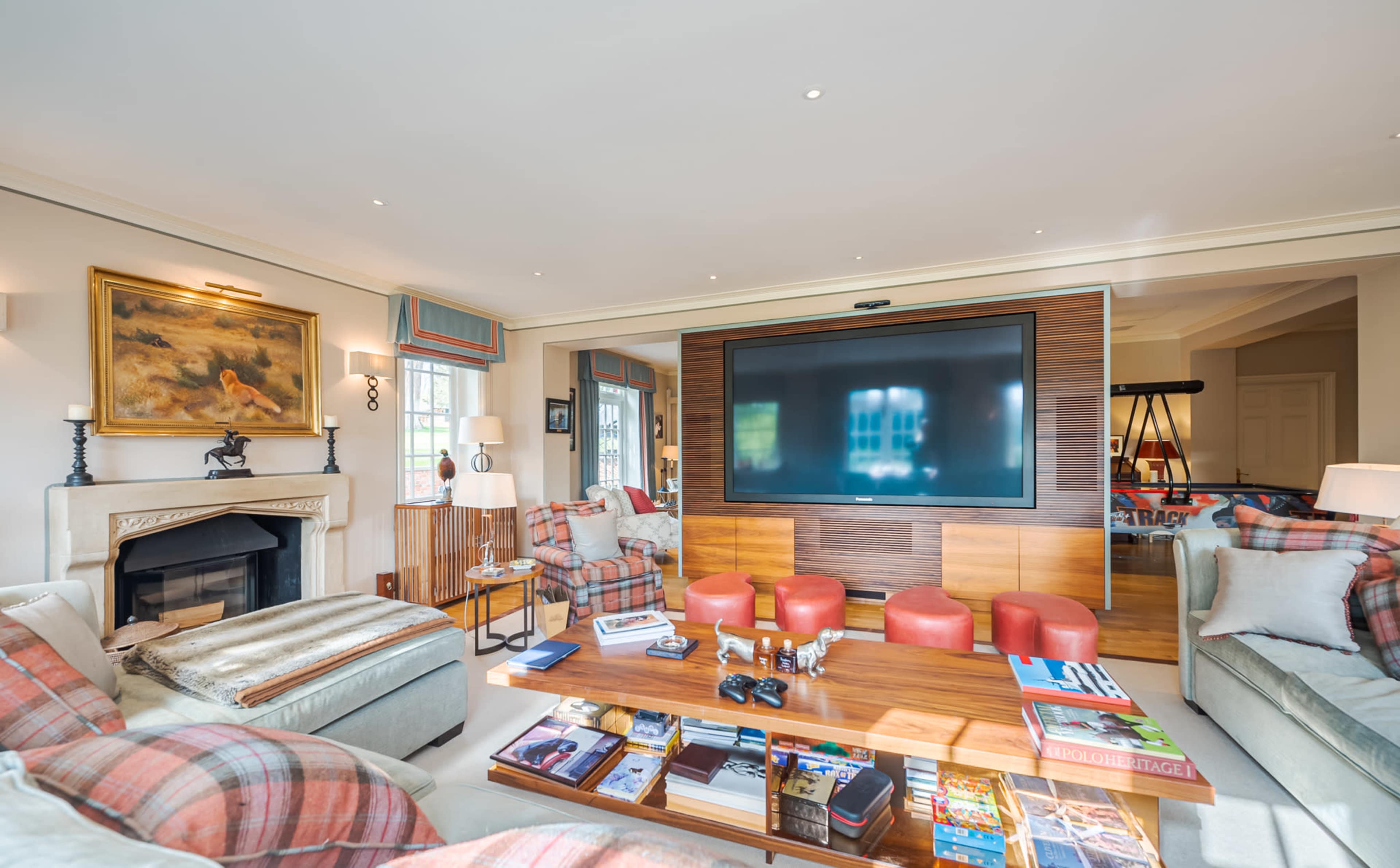 The living room features a fireplace, a large flat-screen television on a wooden panel, and seating arrangements with a coffee table surrounded by chairs and a sofa.