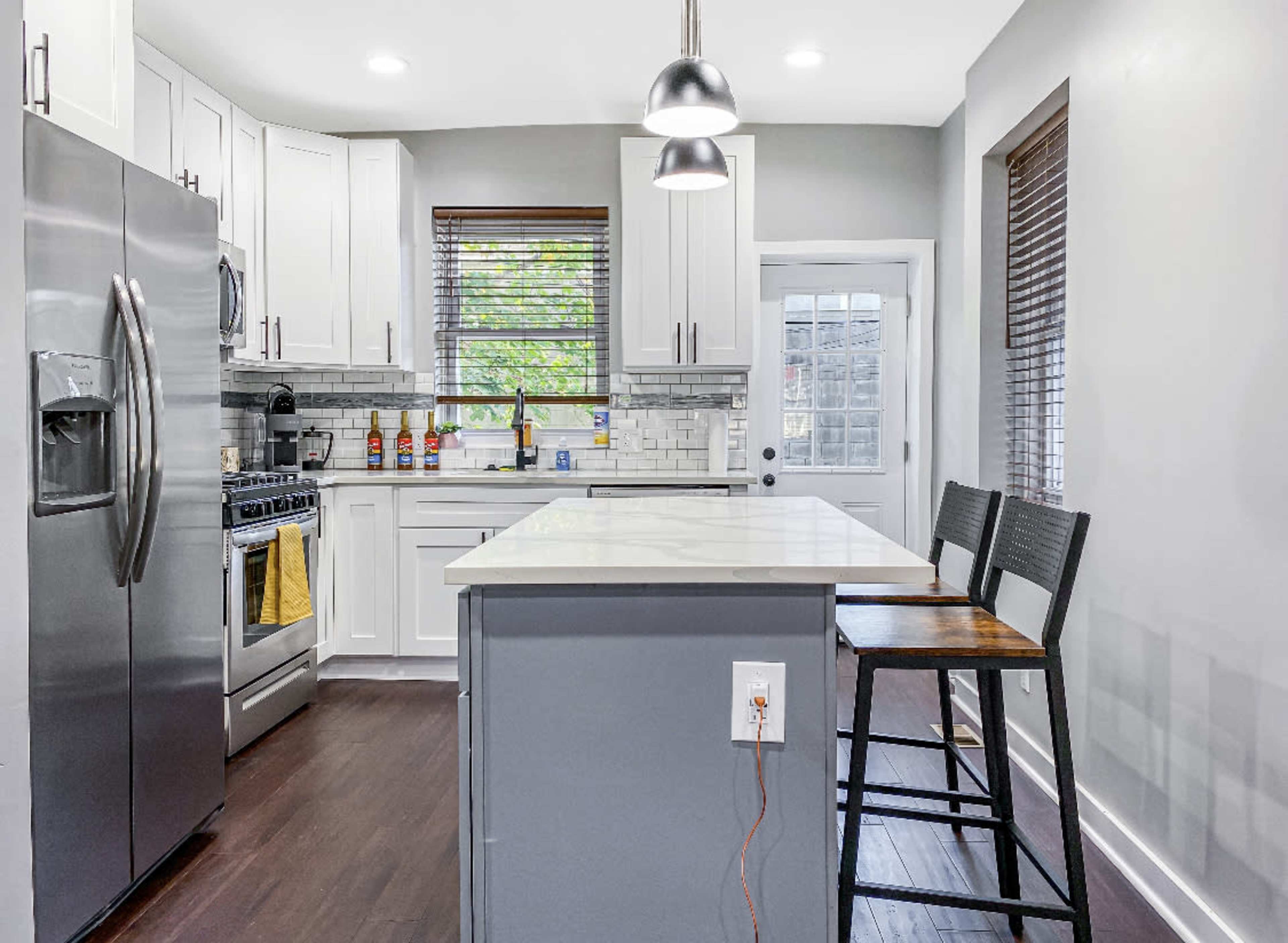 A modern kitchen features stainless steel appliances, white cabinetry, and a central island with bar stools.