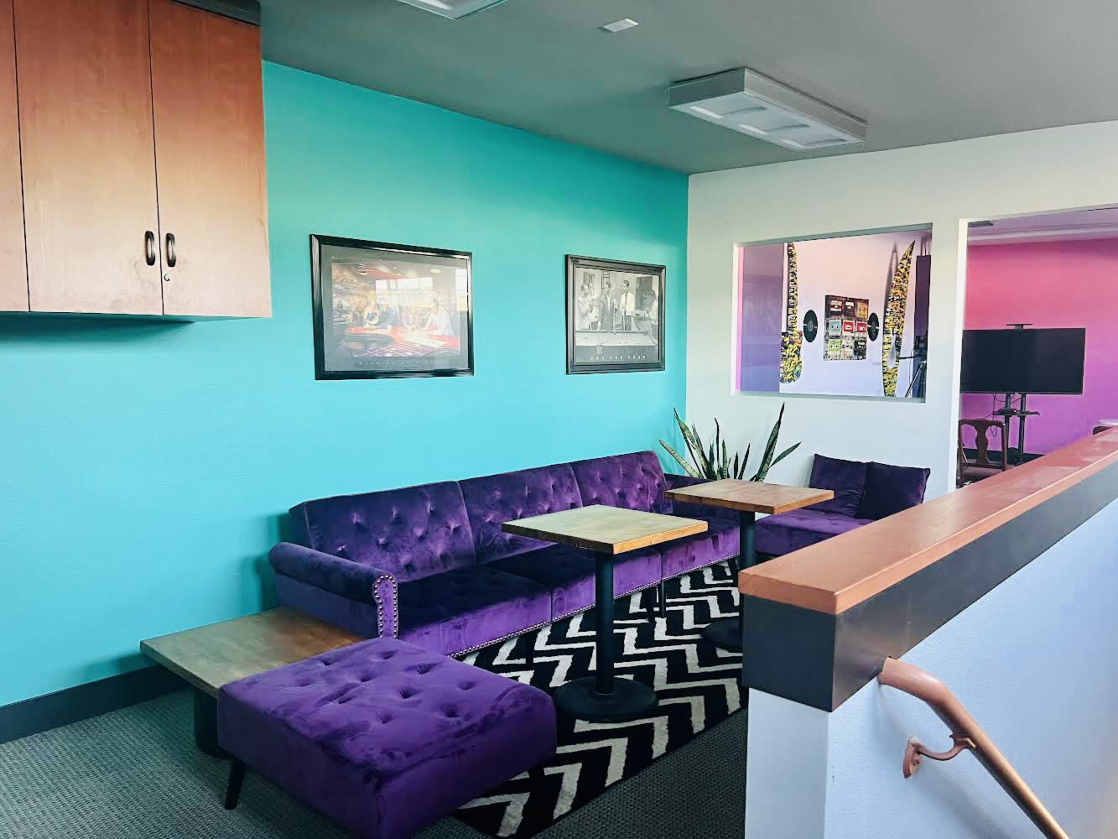 A cozy lounge area featuring a purple velvet sofa, two small tables, and colorful walls with framed artwork.