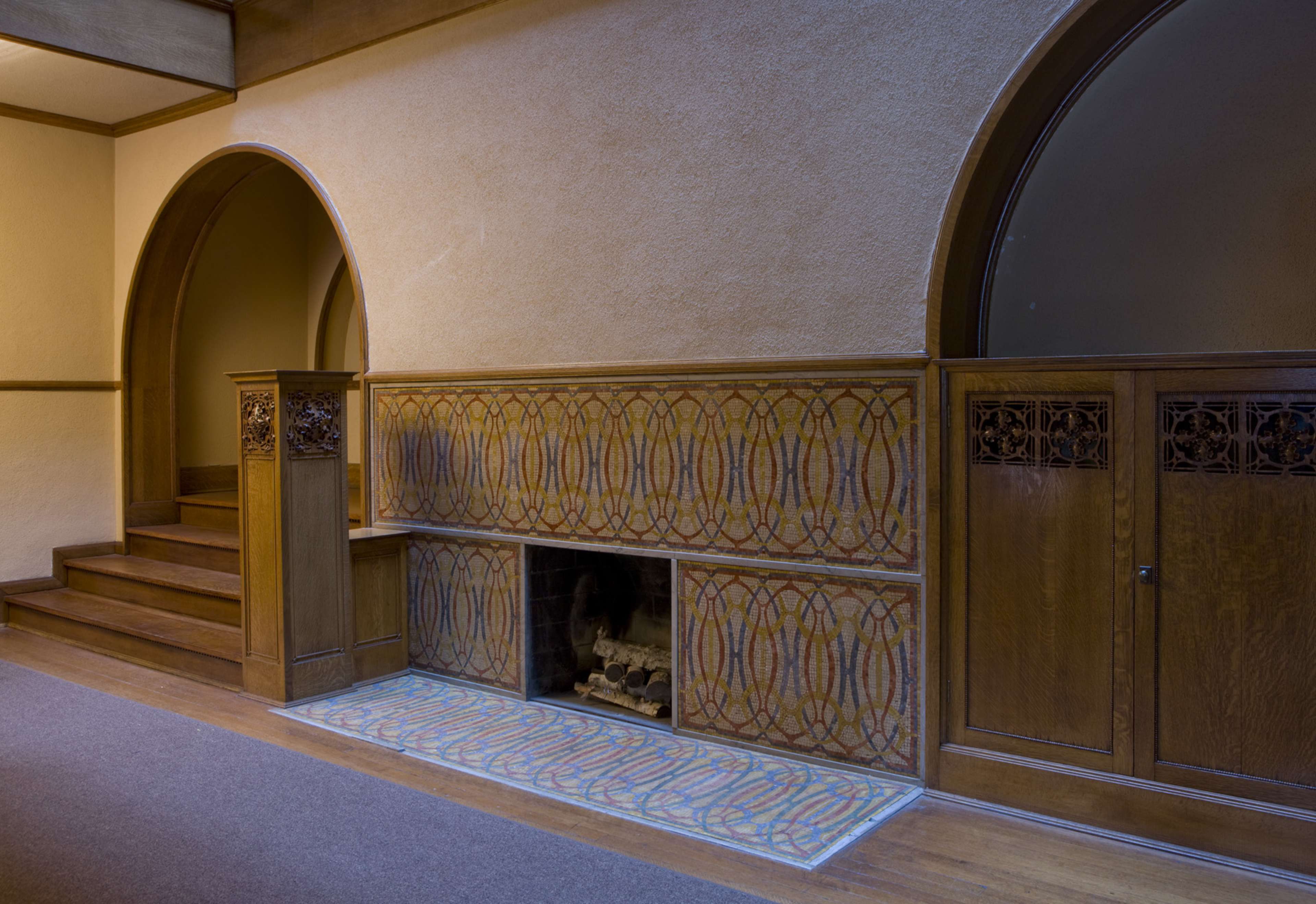 An interior space featuring a staircase, ornate wall detailing, a fireplace, and a decorative tiled hearth.