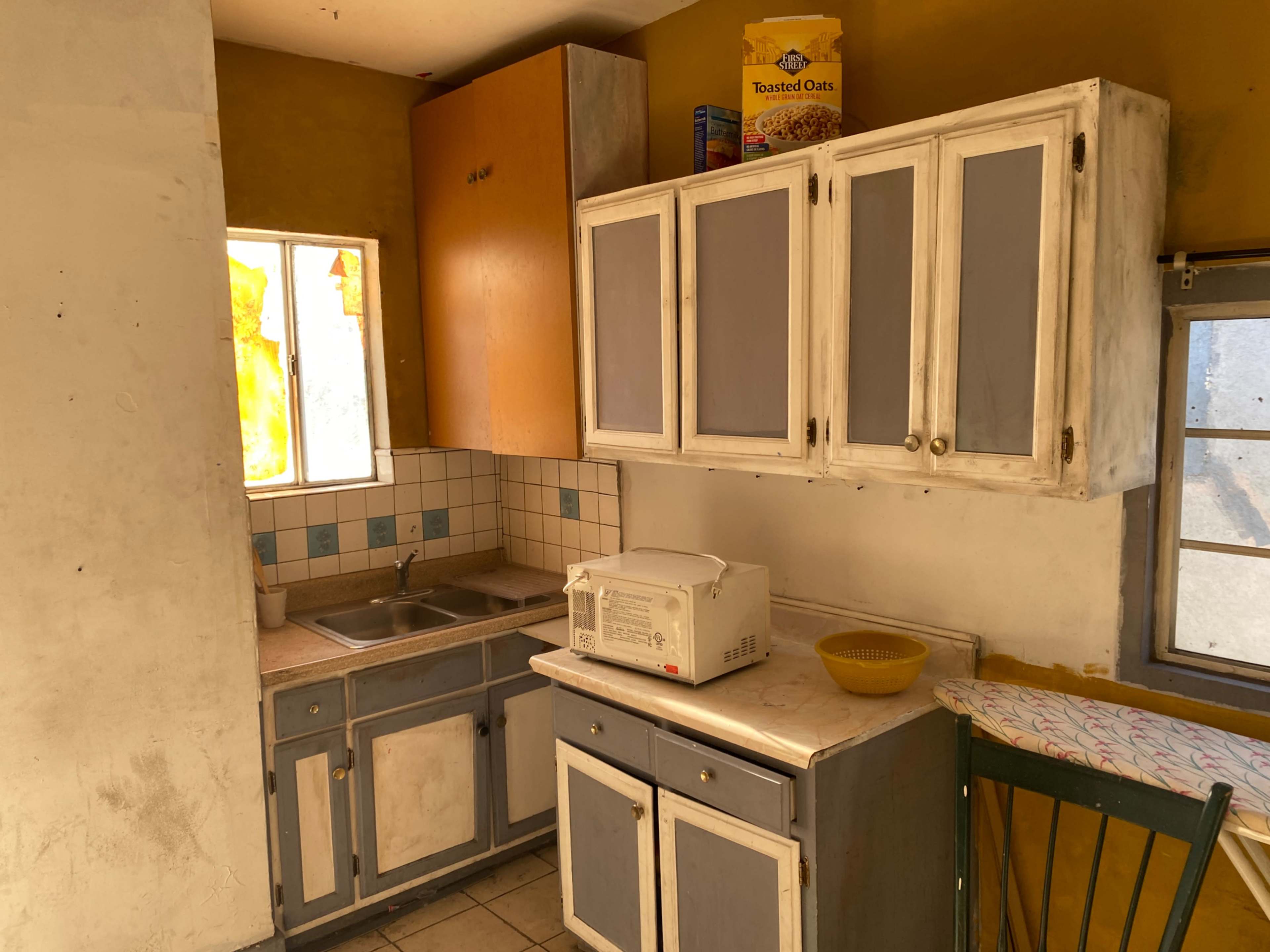 A small kitchen with a sink, microwave, cabinets, and a window, featuring yellow walls and tiled countertops.