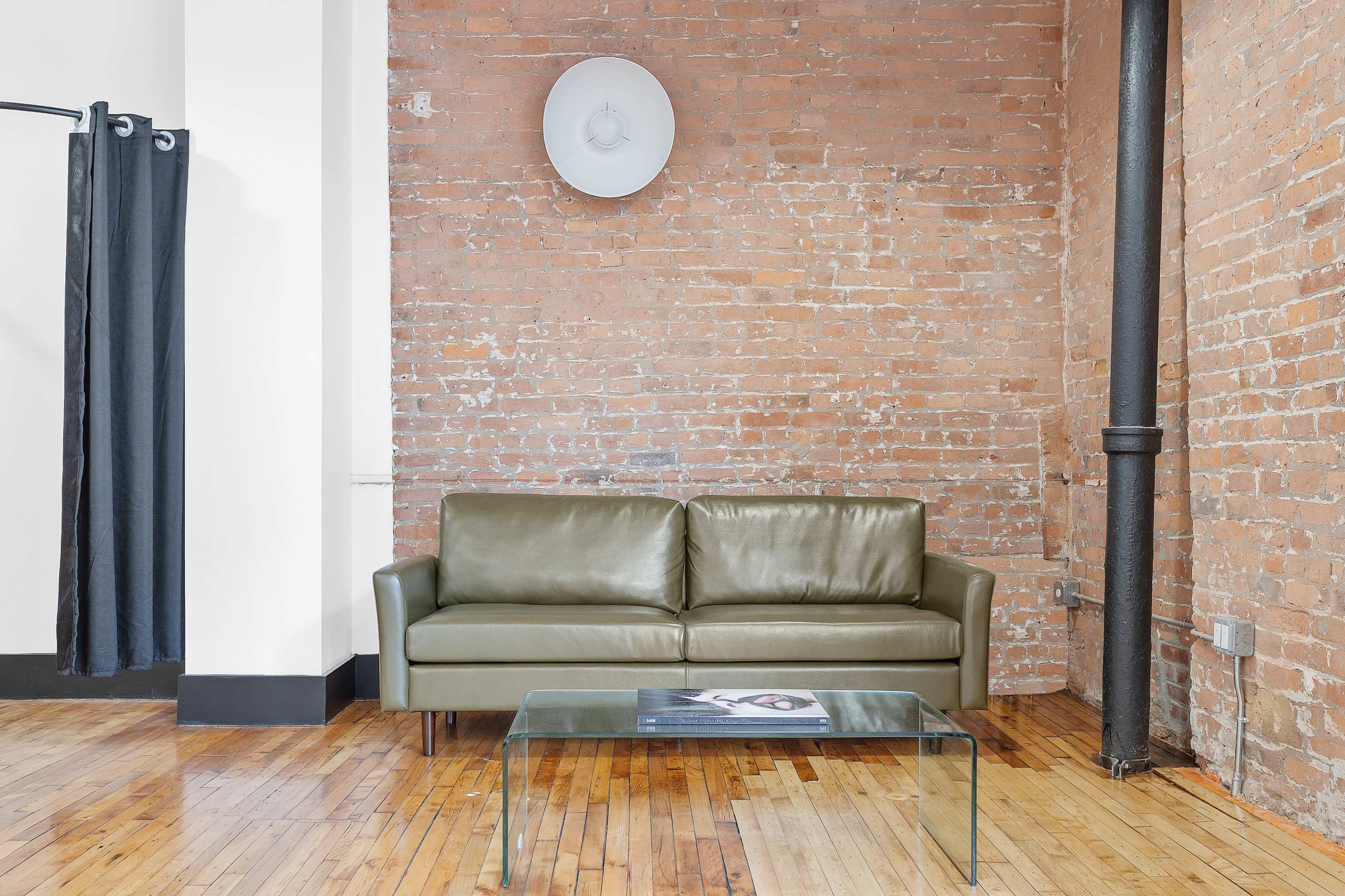 A green sofa and a glass coffee table in a room with exposed brick walls and wooden flooring.