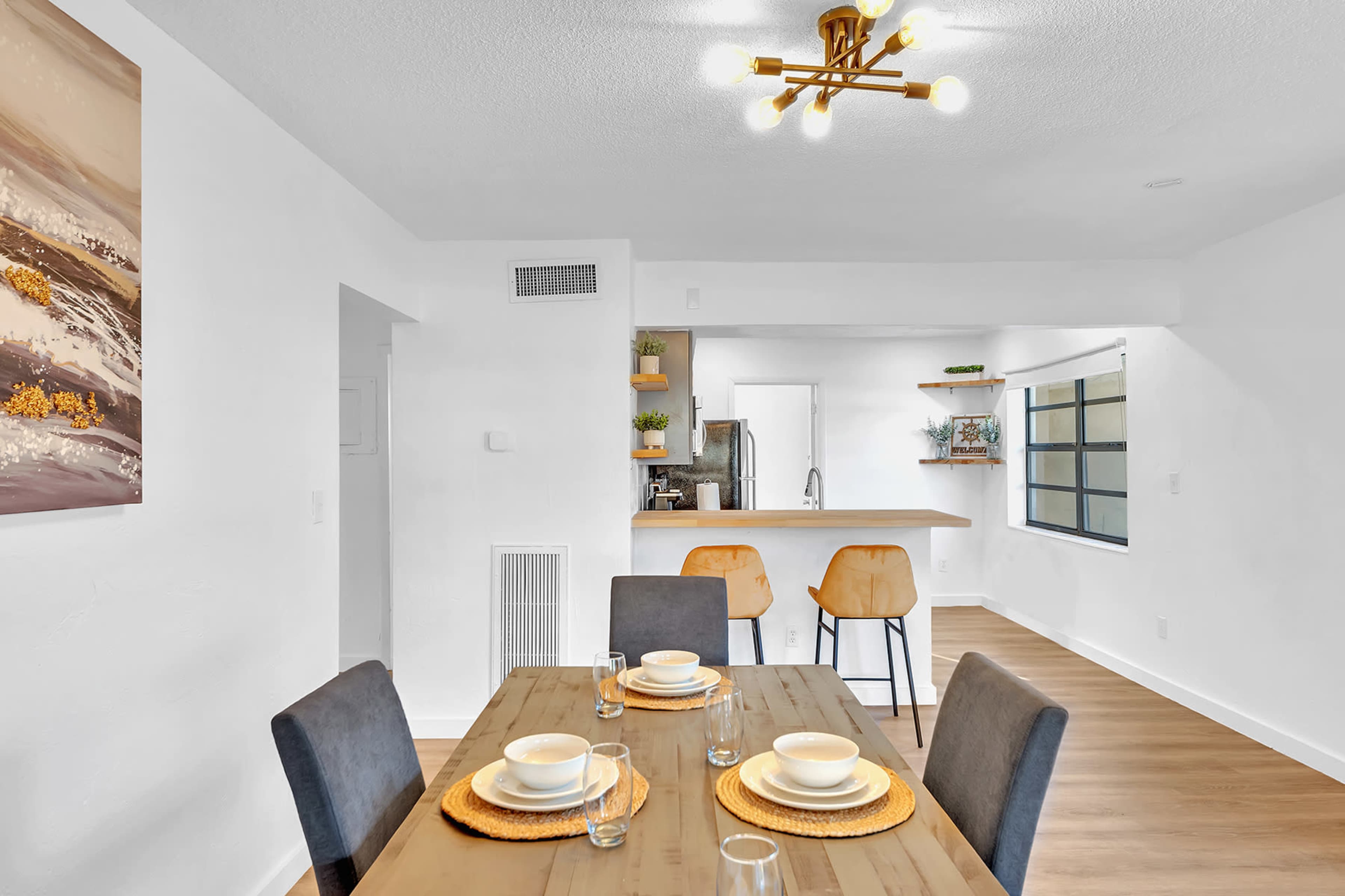 A dining area features a table set for four, with chairs nearby and a kitchen visible in the background.