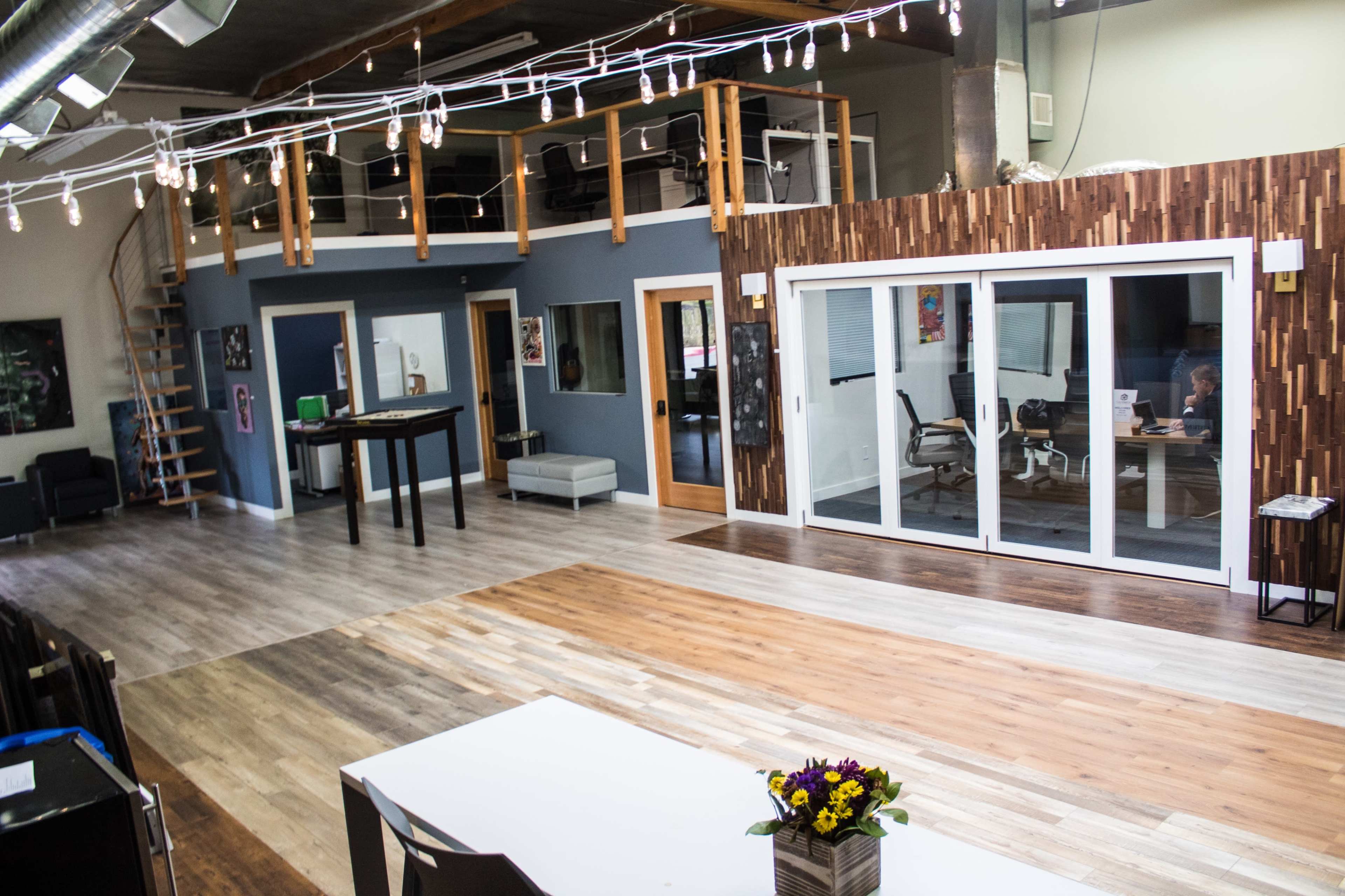 A spacious, modern interior with wooden flooring, multiple doors leading to separate rooms, and a large glass door area that opens to a brightly lit workspace.