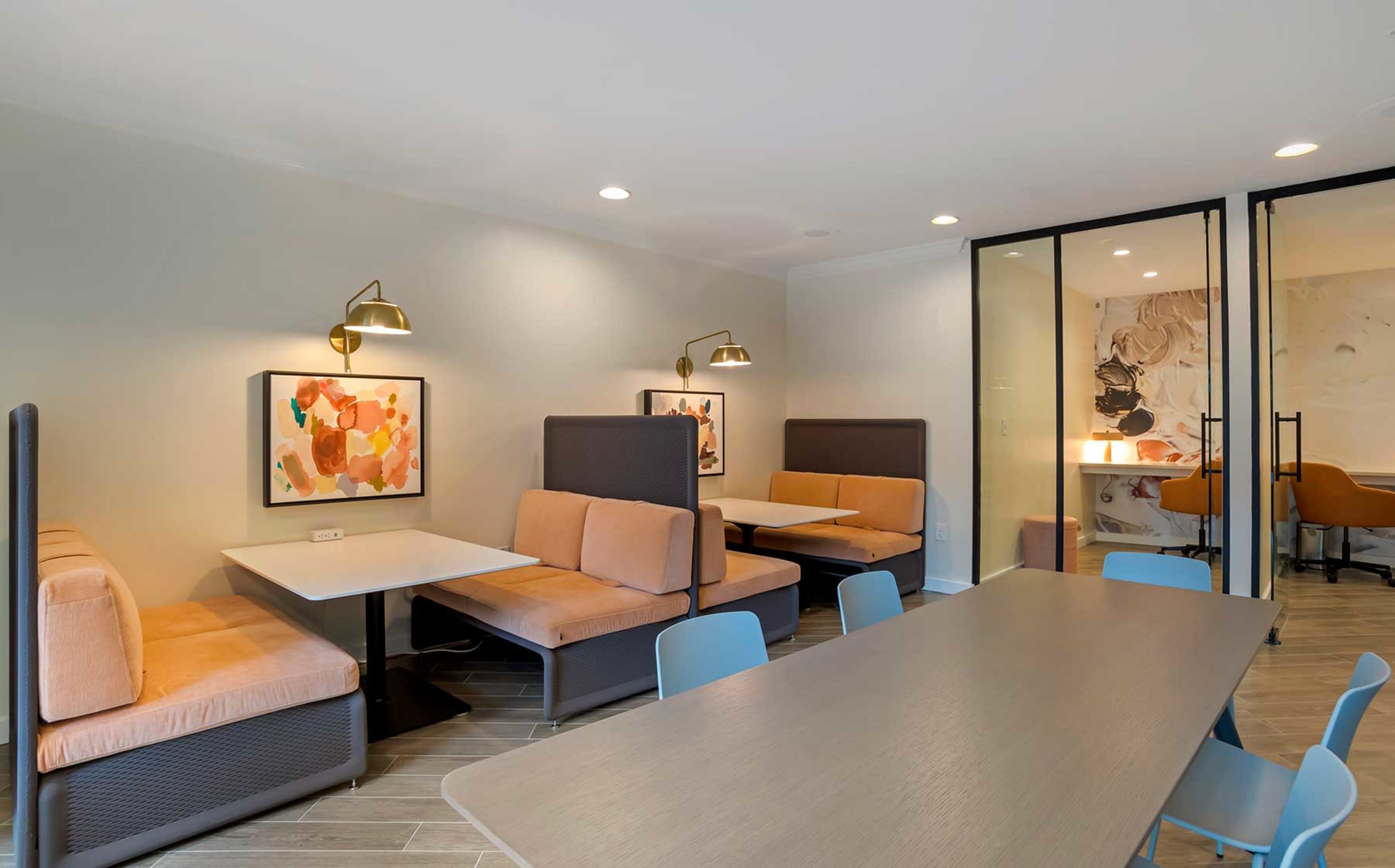 A modern dining area with booth seating and a long table under several overhead lights, featuring artwork on the walls.