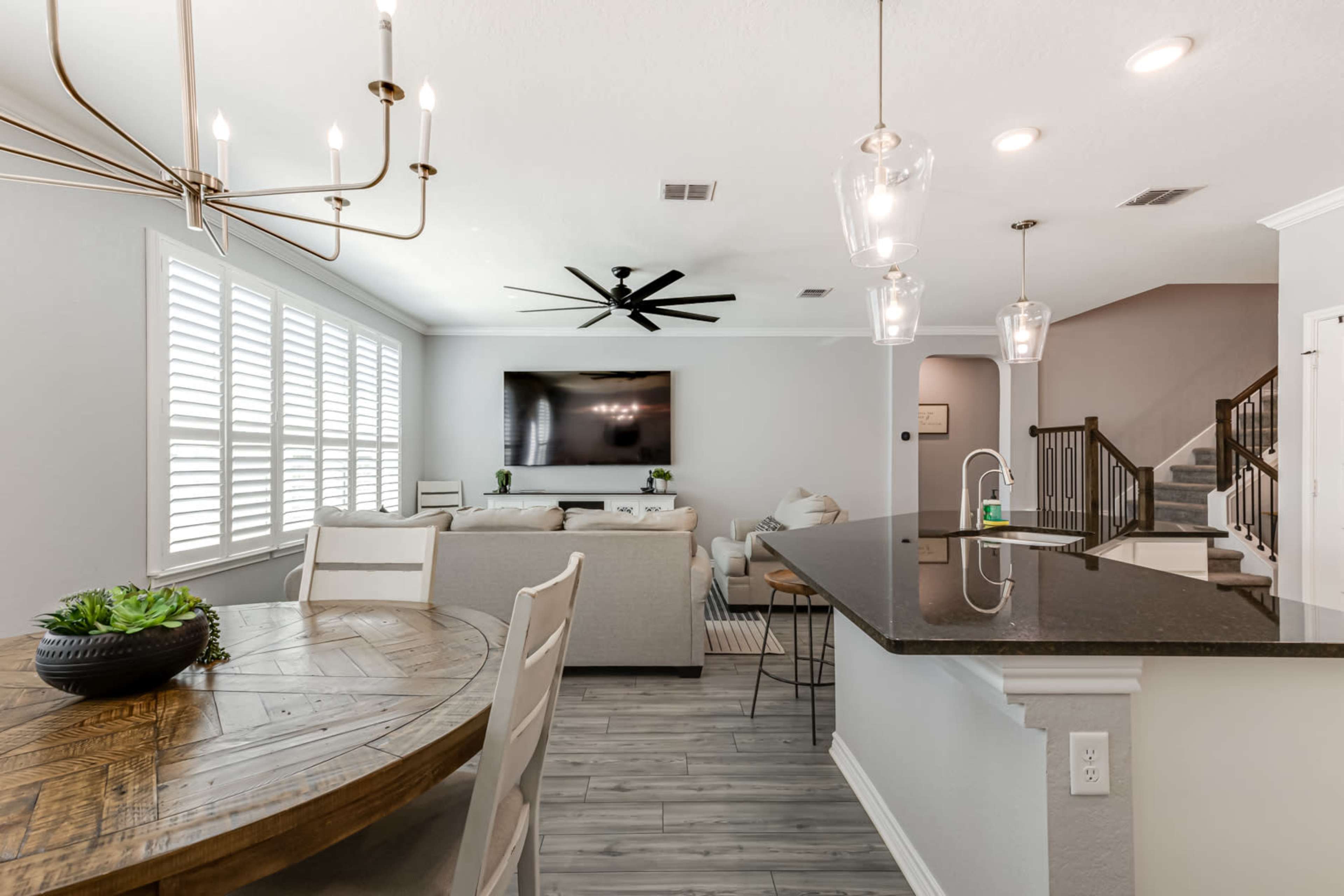 A modern open-concept living area with a dining space, a kitchen island, and a seating area equipped with a large television mounted on the wall.