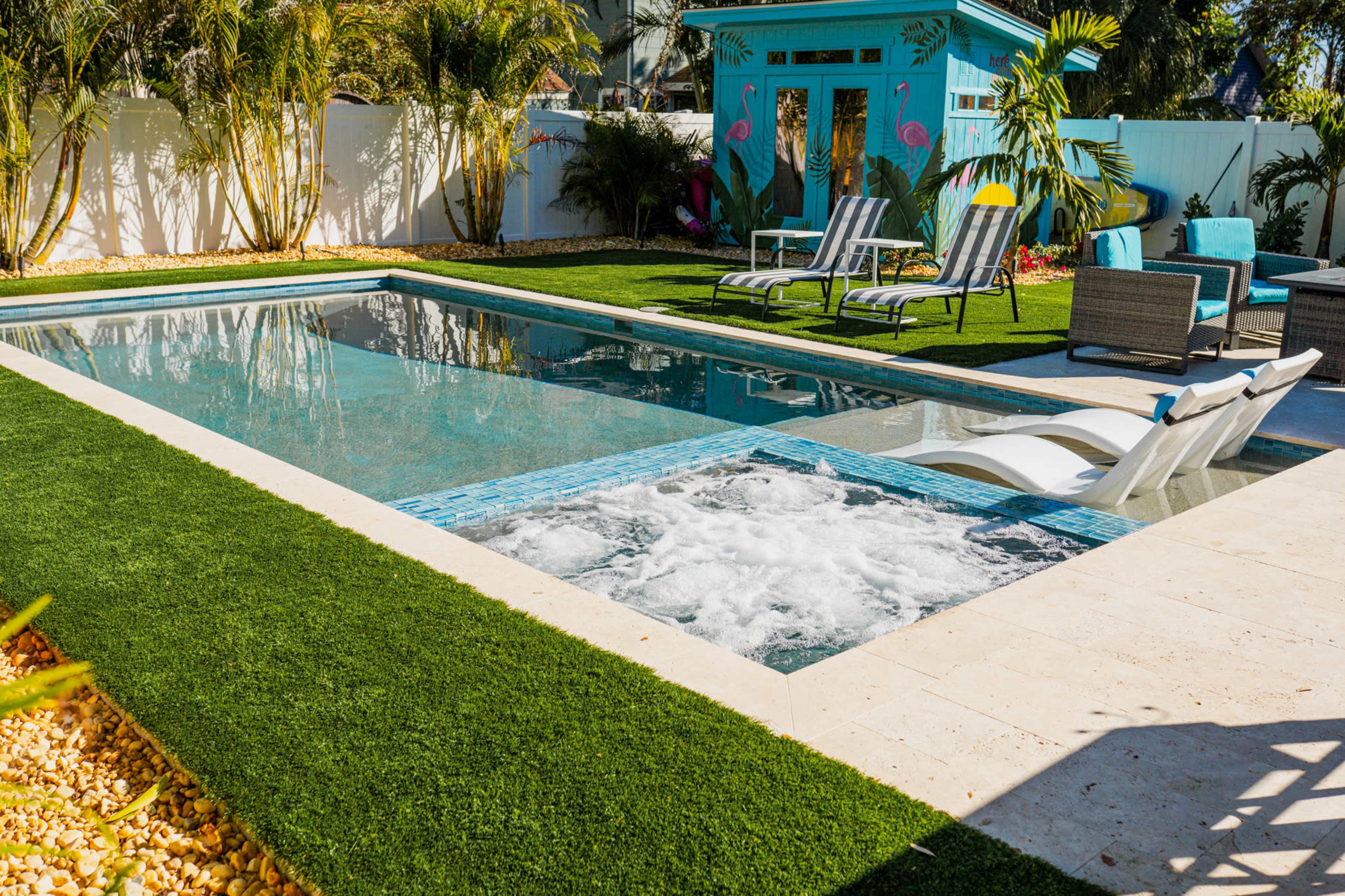 A backyard swimming pool area featuring a hot tub, lounge chairs, and vibrant landscaping.
