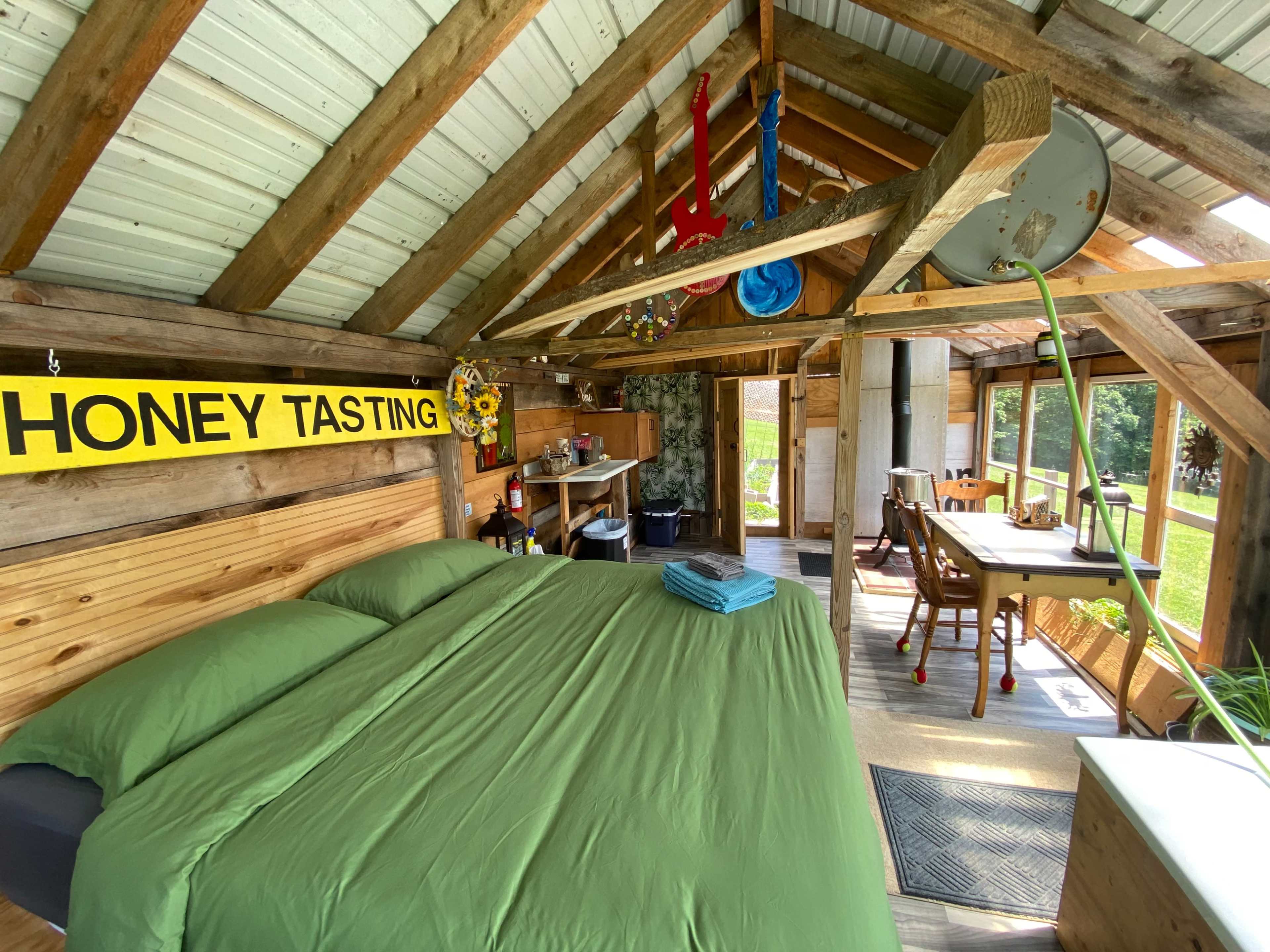 The image shows a rustic interior of a wooden cabin featuring a bed, a dining area, and a sign that reads "HONEY TASTING."
