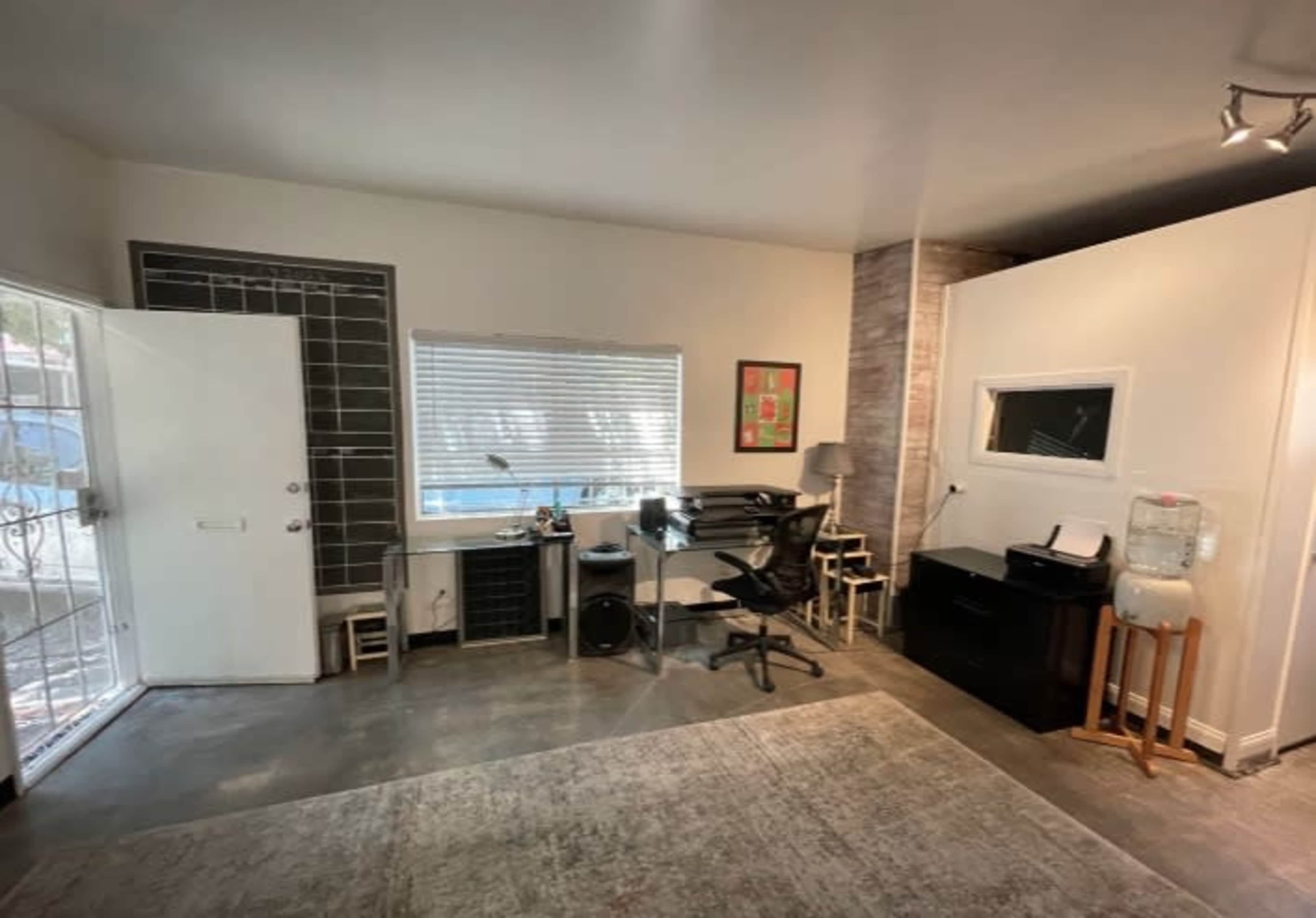 A modern office space features a desk and chair, a water cooler, and a large window allowing natural light.