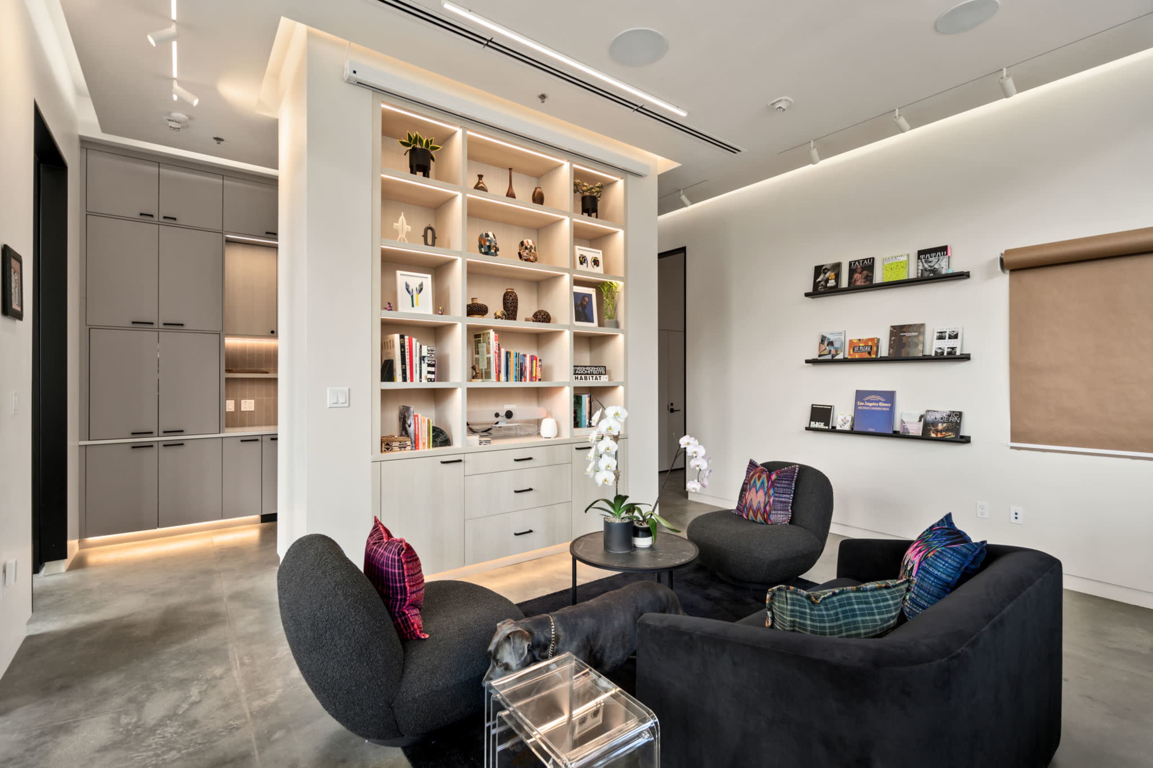 A modern living area features two black chairs, a circular table, and a built-in shelving unit displaying books and decorative items.