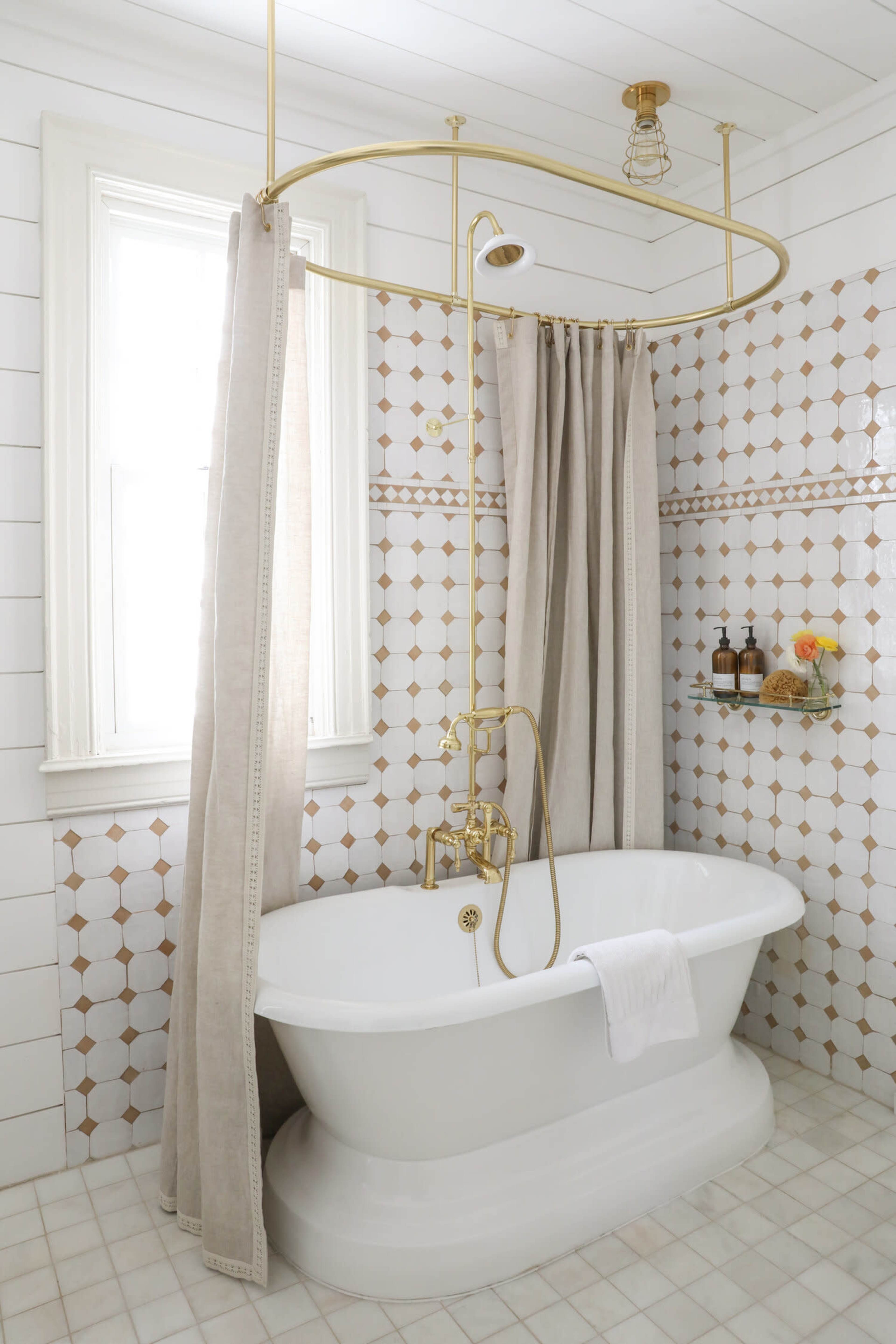 A bathroom featuring a freestanding white bathtub, a gold shower fixture, and a tiled wall with a geometric pattern.