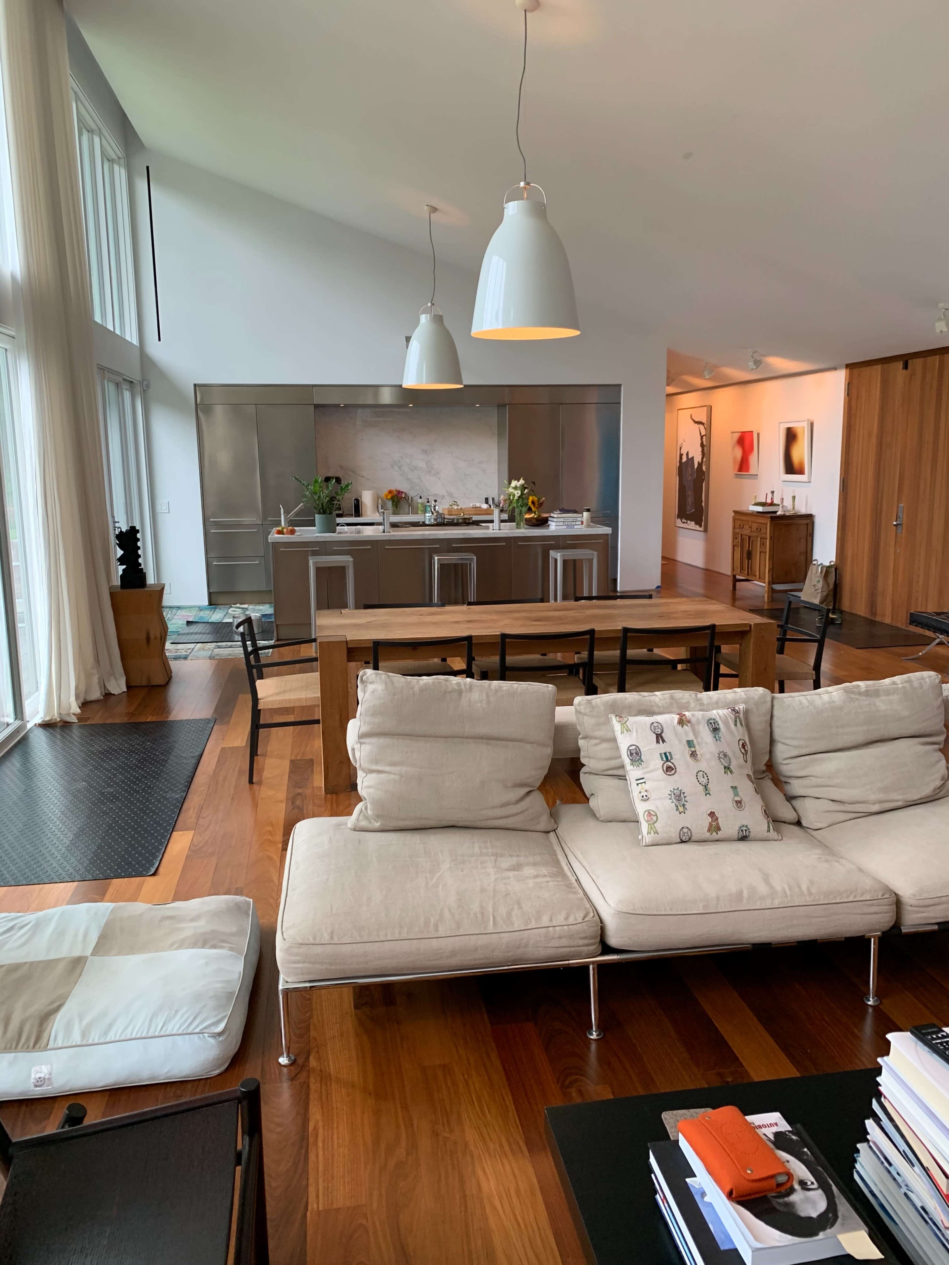 A modern open-concept living area features a sectional sofa in the foreground and a kitchen with stainless steel appliances in the background.
