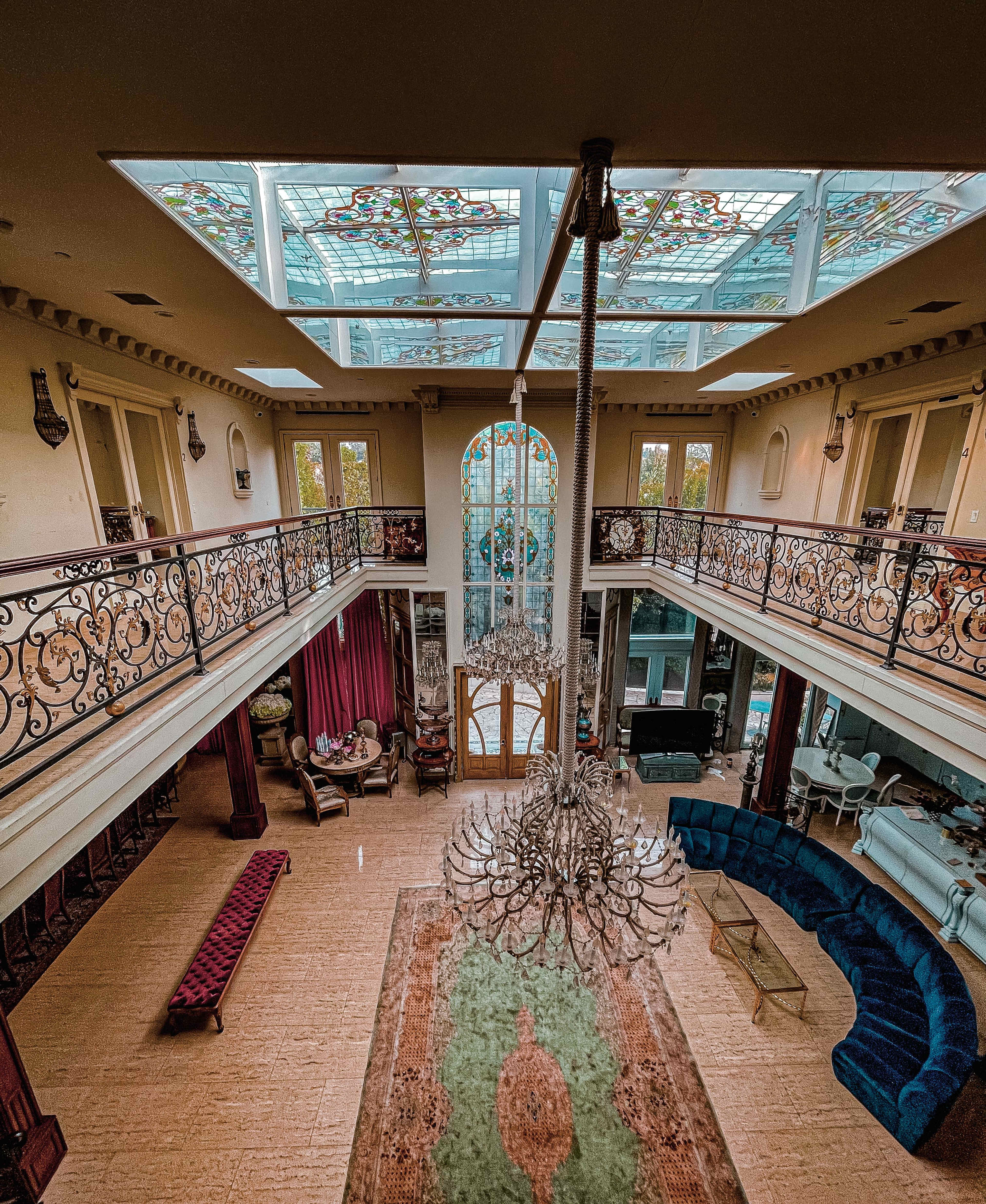 A spacious, two-story living area with a large chandelier, ornate railings, and a stained glass skylight.
