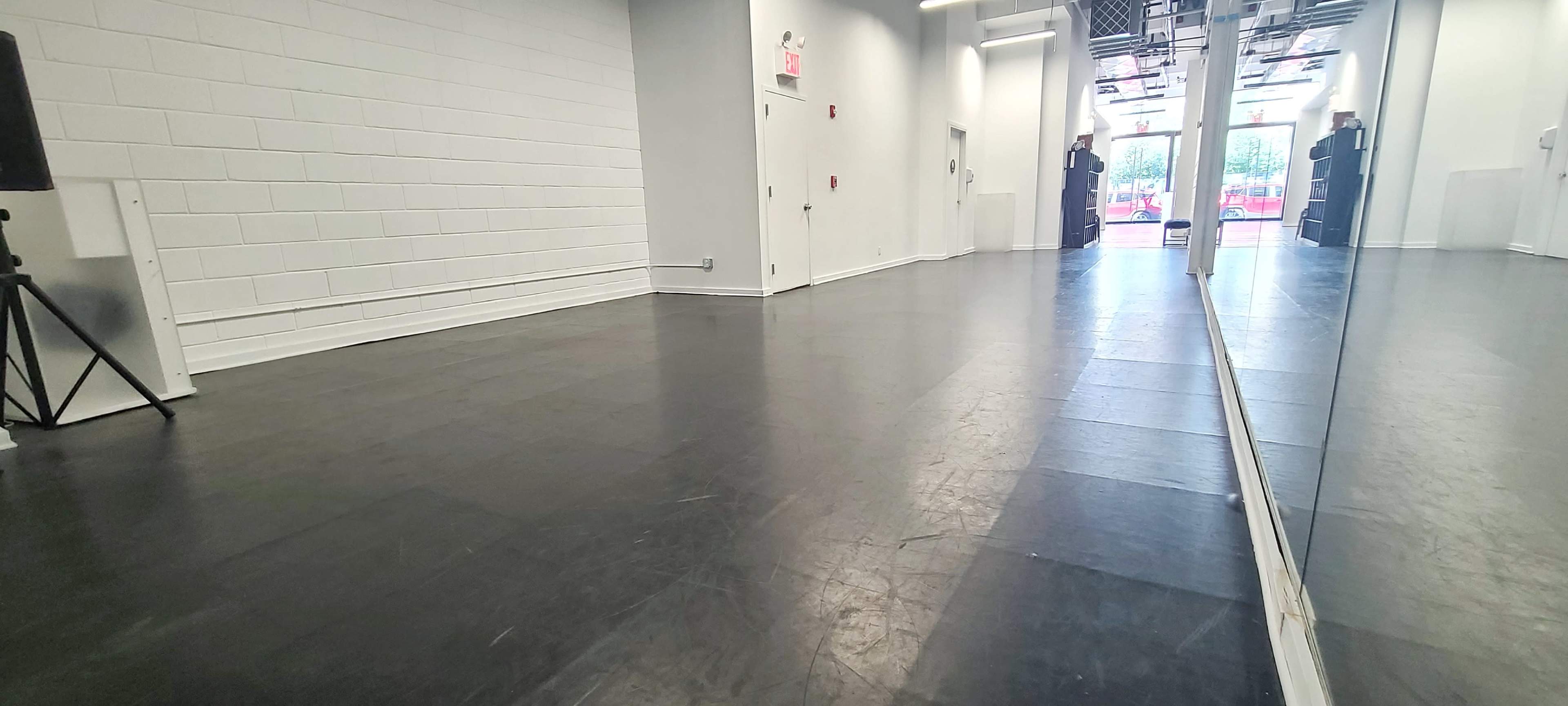 A spacious, empty room with black flooring and large mirrors along one wall, leading to an entrance with doors.