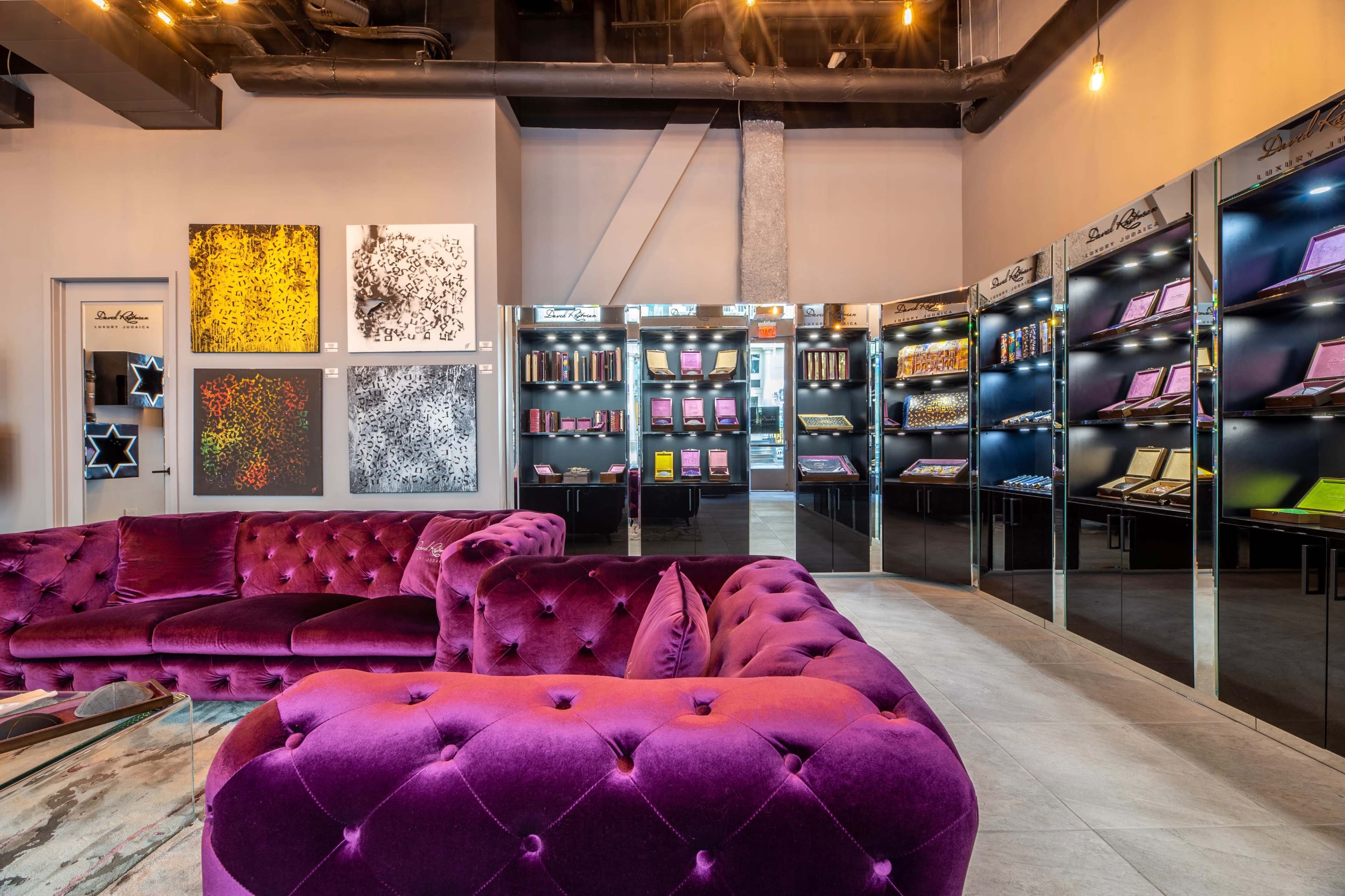 A modern interior features a plush purple couch in front of wall displays showcasing various products and artwork.
